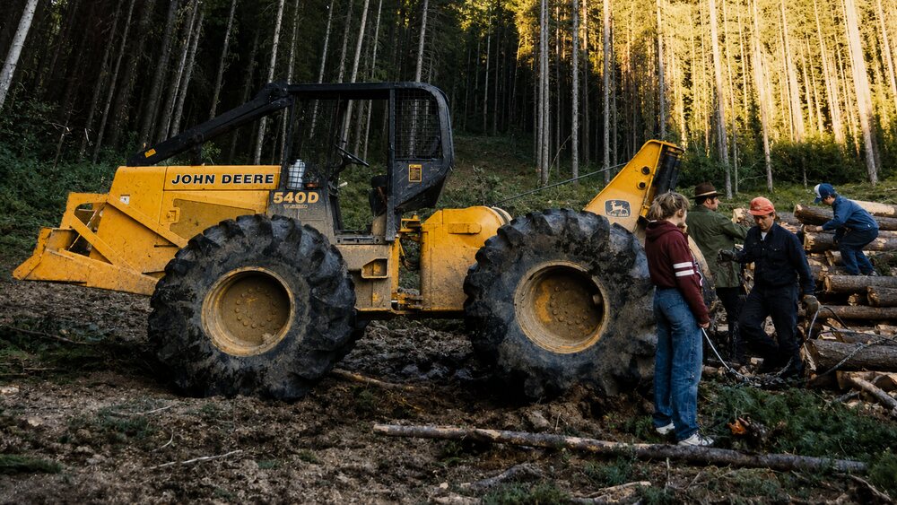 Family background photograph showing forestry equipment and people in a wooded work area.