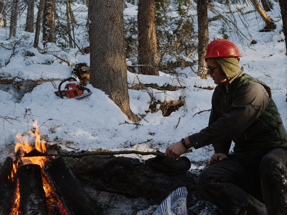 Family background photograph showing Joel's father in winter woods near a small fire and timber work.