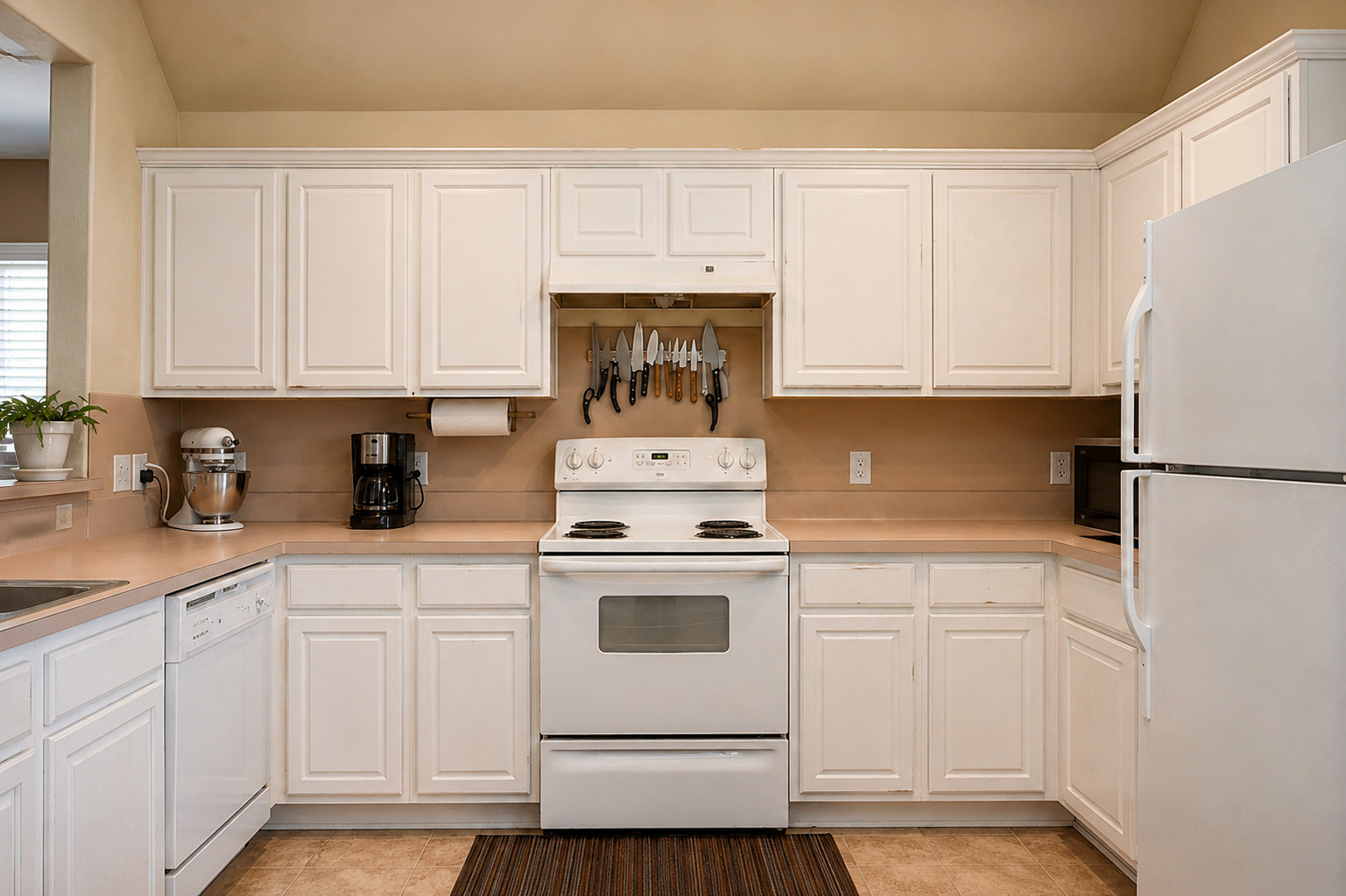 Before view of a white kitchen with upper cabinets, central range, refrigerator at right, and matching U-shaped cabinet layout.