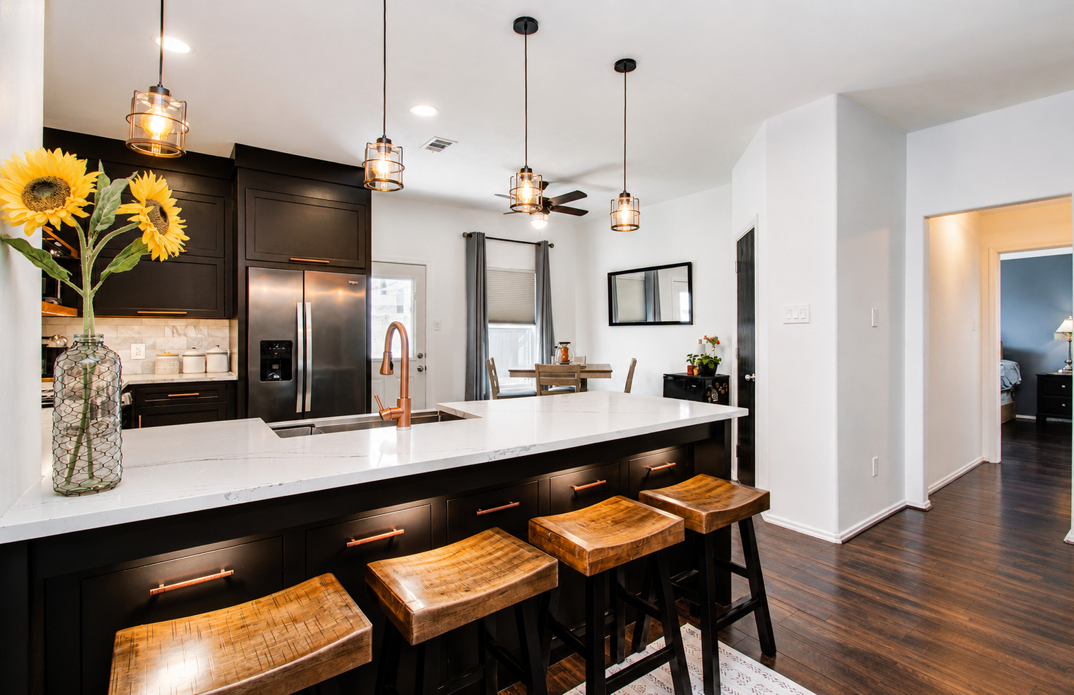 Wide side view of finished dark kitchen with island seating, wood shelves, range wall, and adjacent living space.