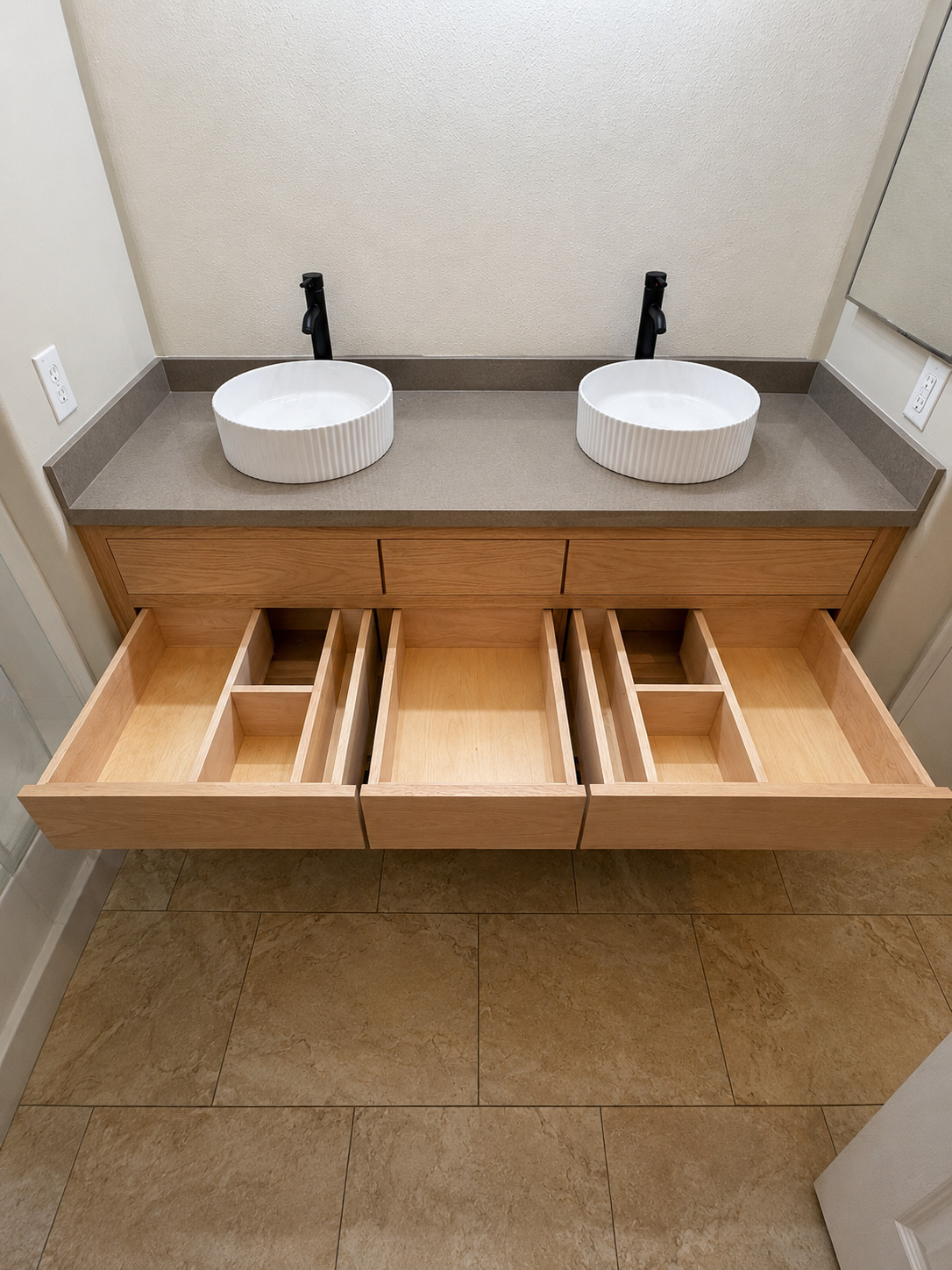 Light wood double vanity with open drawers, vessel sinks, tall backsplash, and plumbing fixtures.