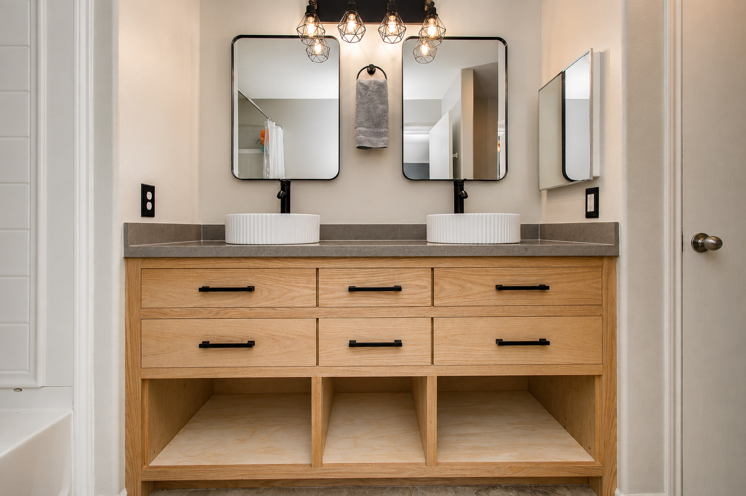 Light wood vanity with drawers, open lower shelf, stone counter, wall-mounted faucet, and mirrored cabinets.