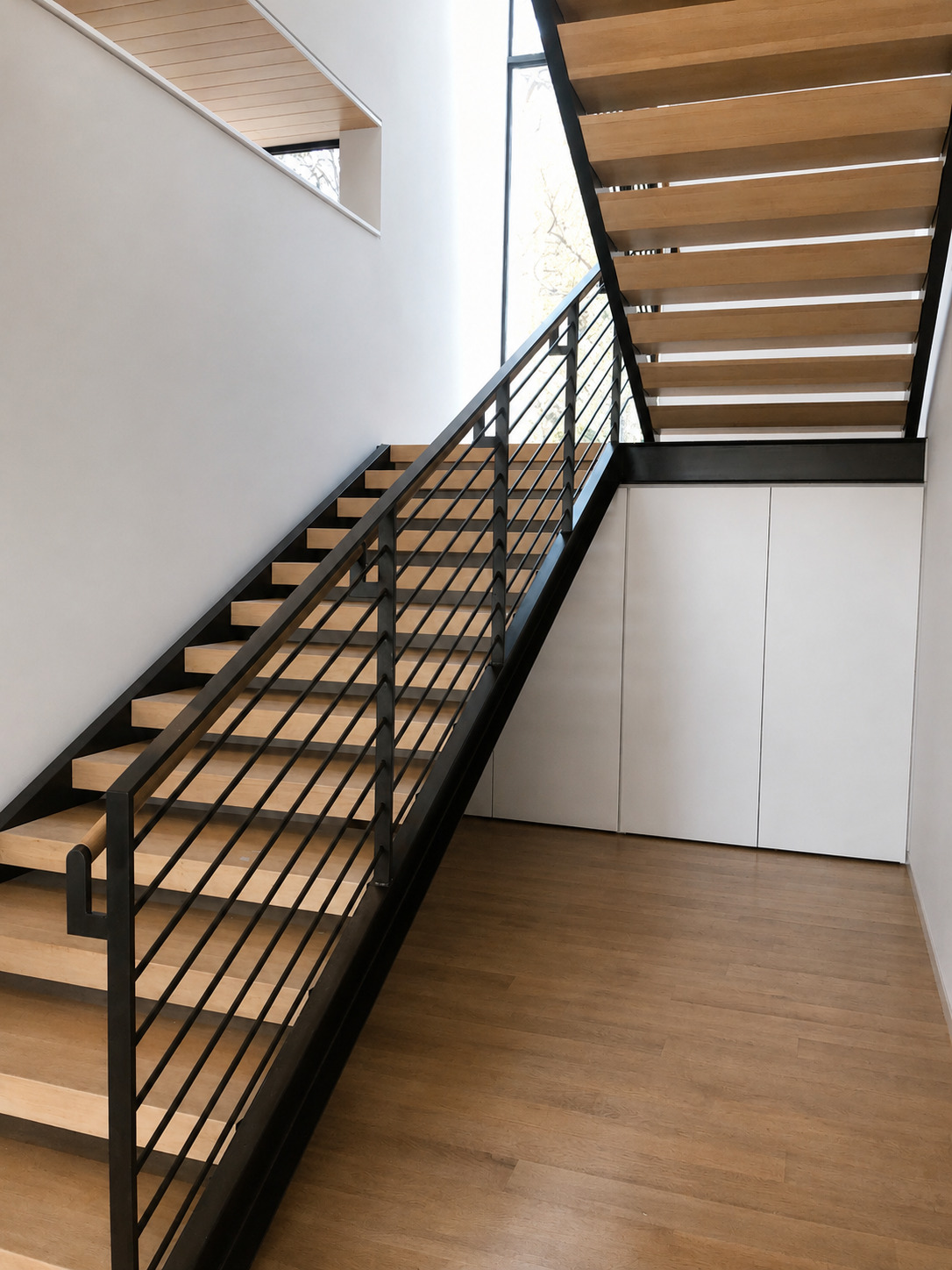Angled stair view with light wood treads, dark steel railings, white walls, and wall lights.