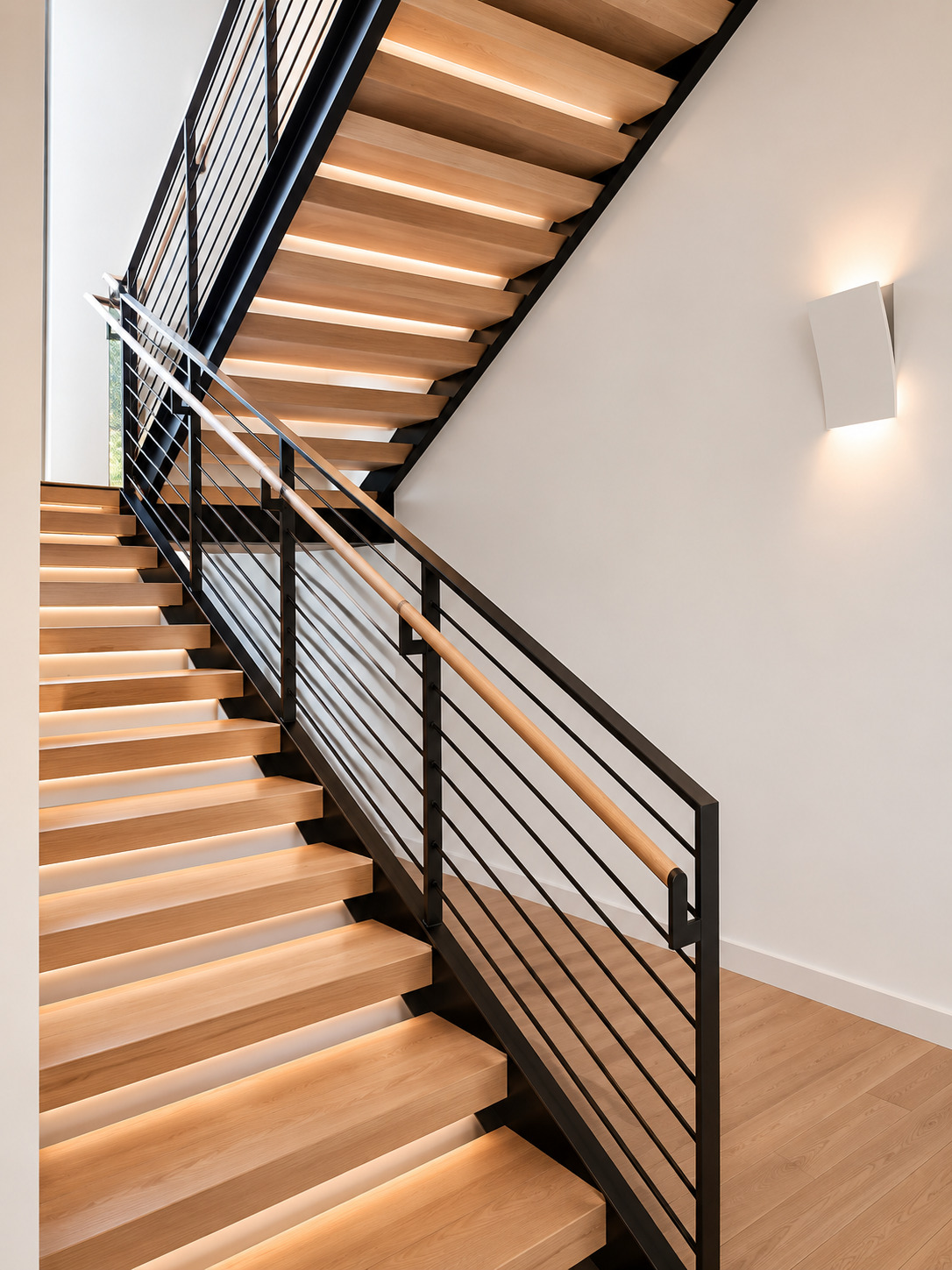 Wide stair view with light wood treads, dark steel railings, lower storage wall, and white walls.