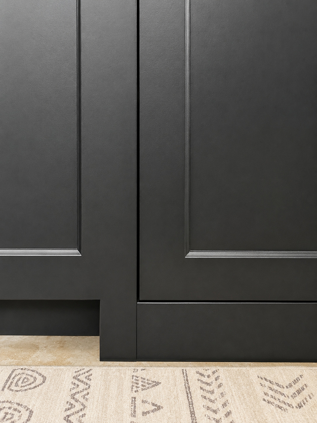 Close view of dark base cabinet doors aligned above a toe-kick area at the finished floor line.