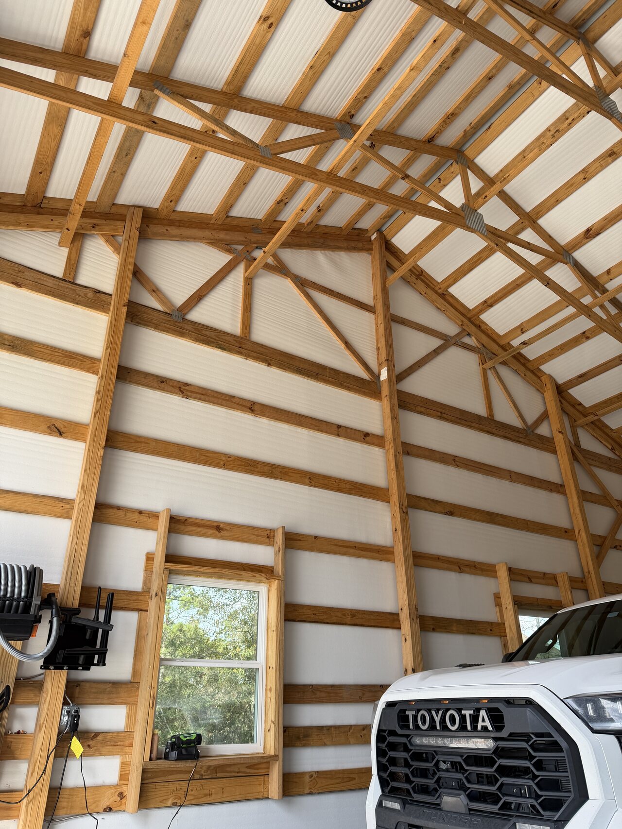 Wide finished barn interior with exposed wood trusses, horizontal wall boards, windows, and open concrete floor.