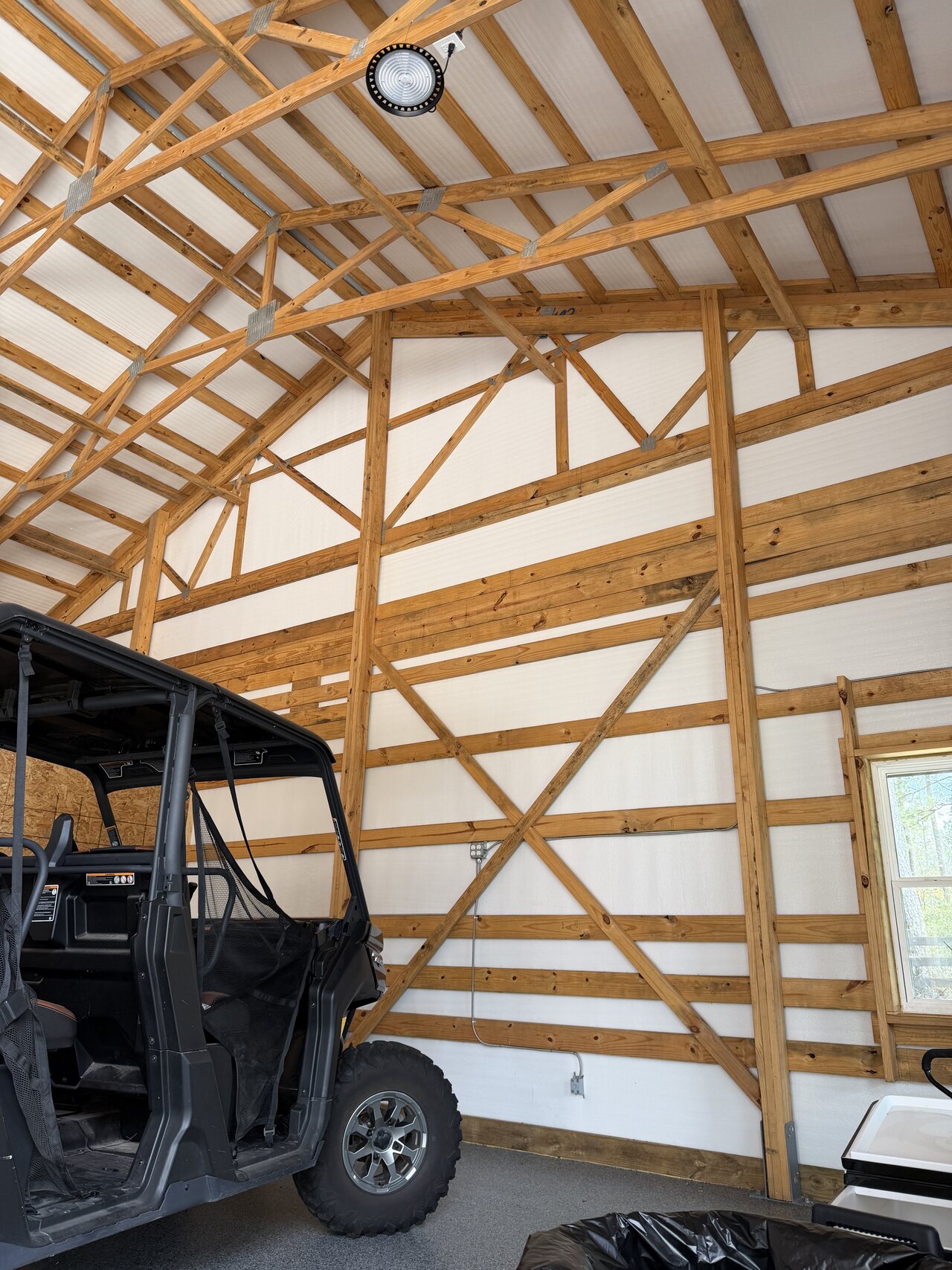 Finished barn interior corner with roof trusses, wood wall pattern, utility vehicle, and side wall openings.