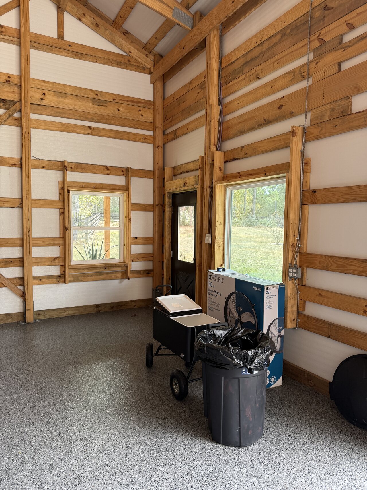 Finished barn corner with window trim, natural wood rails, lower panels, and open concrete floor.