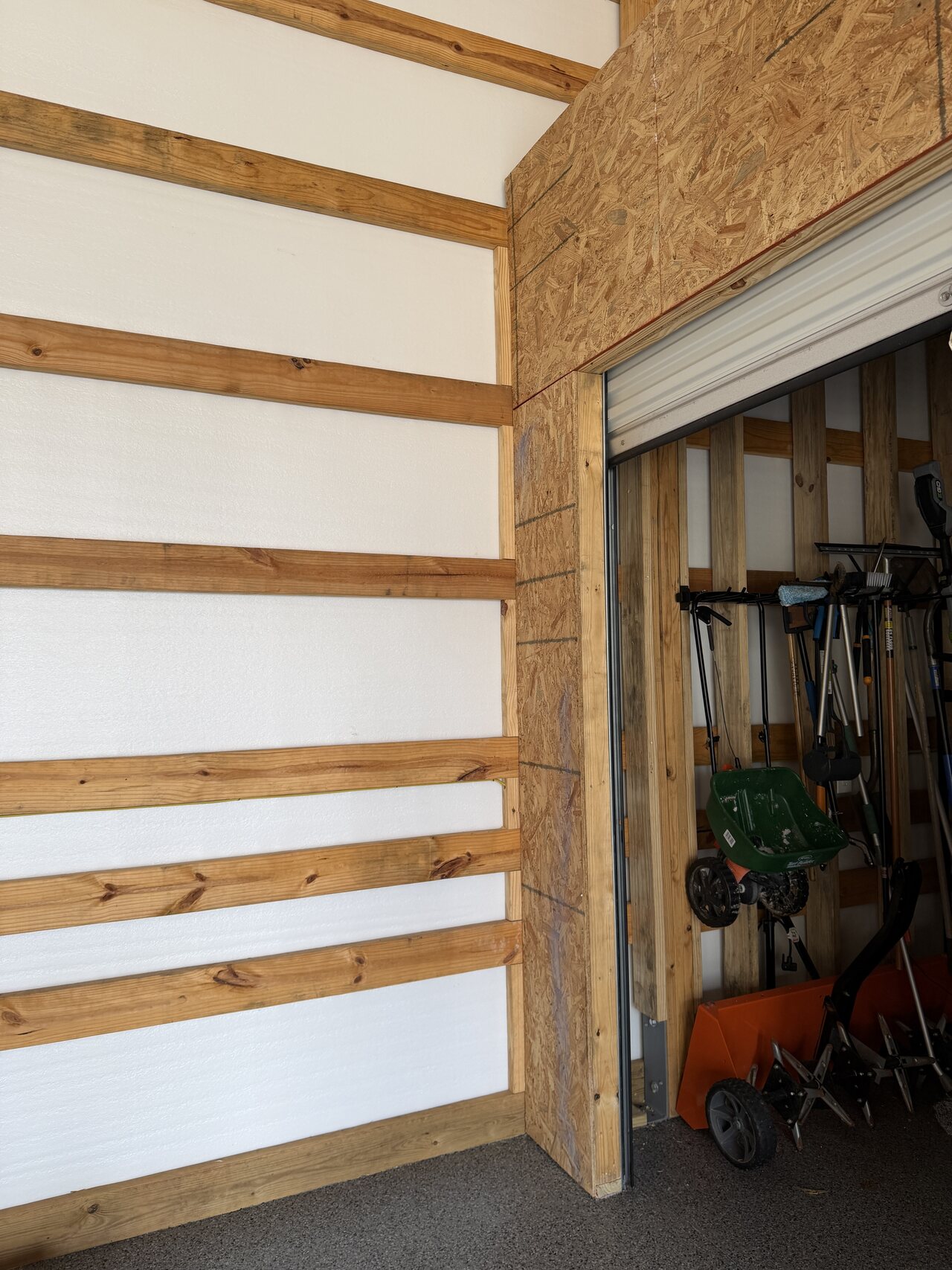 OSB-framed roll-up opening integrated with adjacent horizontal wood rails on a barn wall.