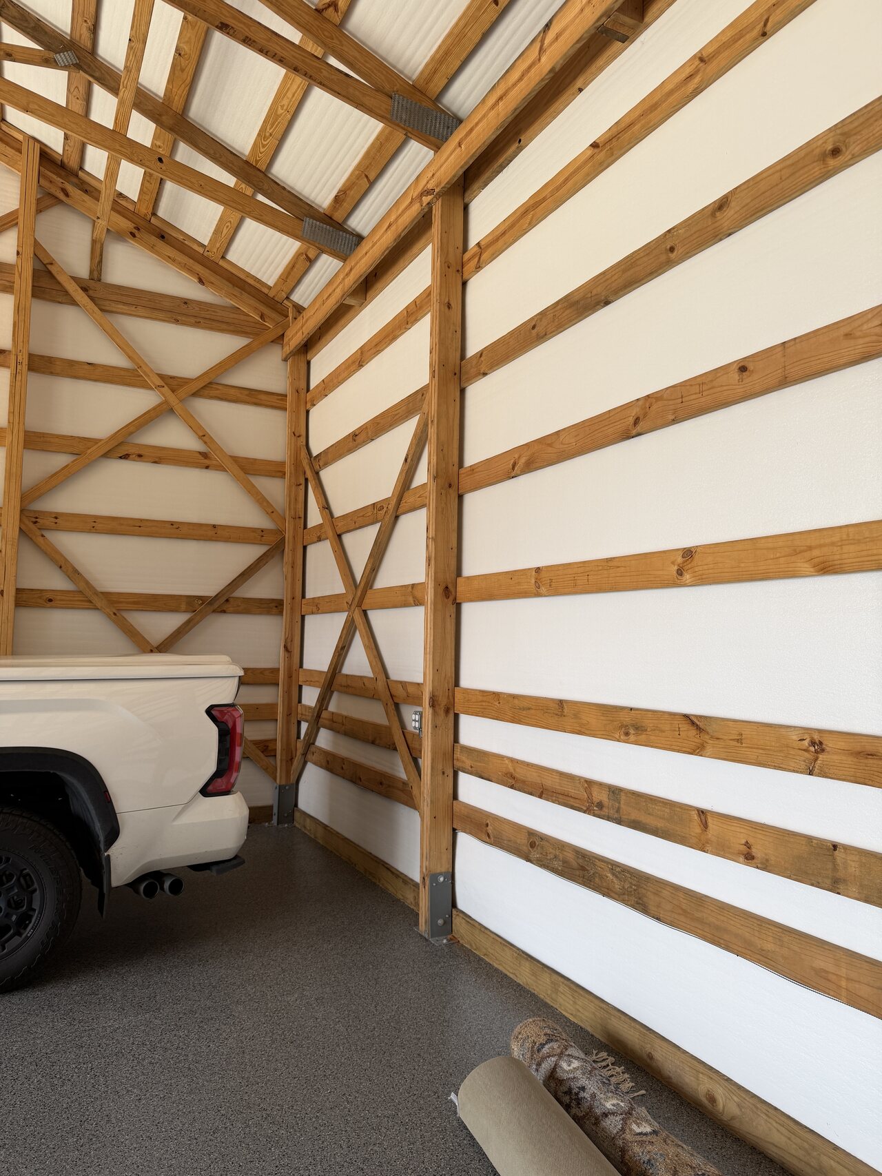 Tall barn wall bay with diagonal bracing, repeated horizontal wood boards, and white wall panels.