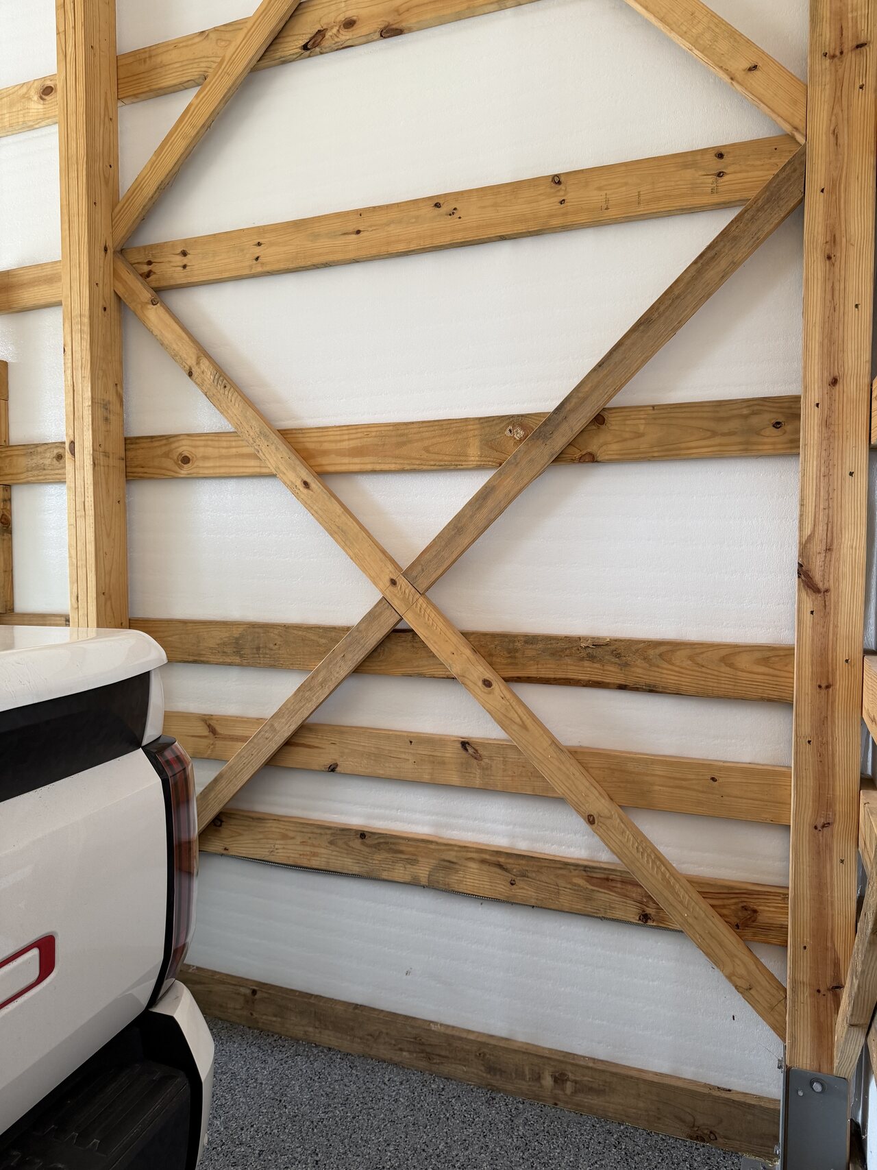 X-braced barn wall panel with natural wood battens, lower rail work, and concrete floor transition.