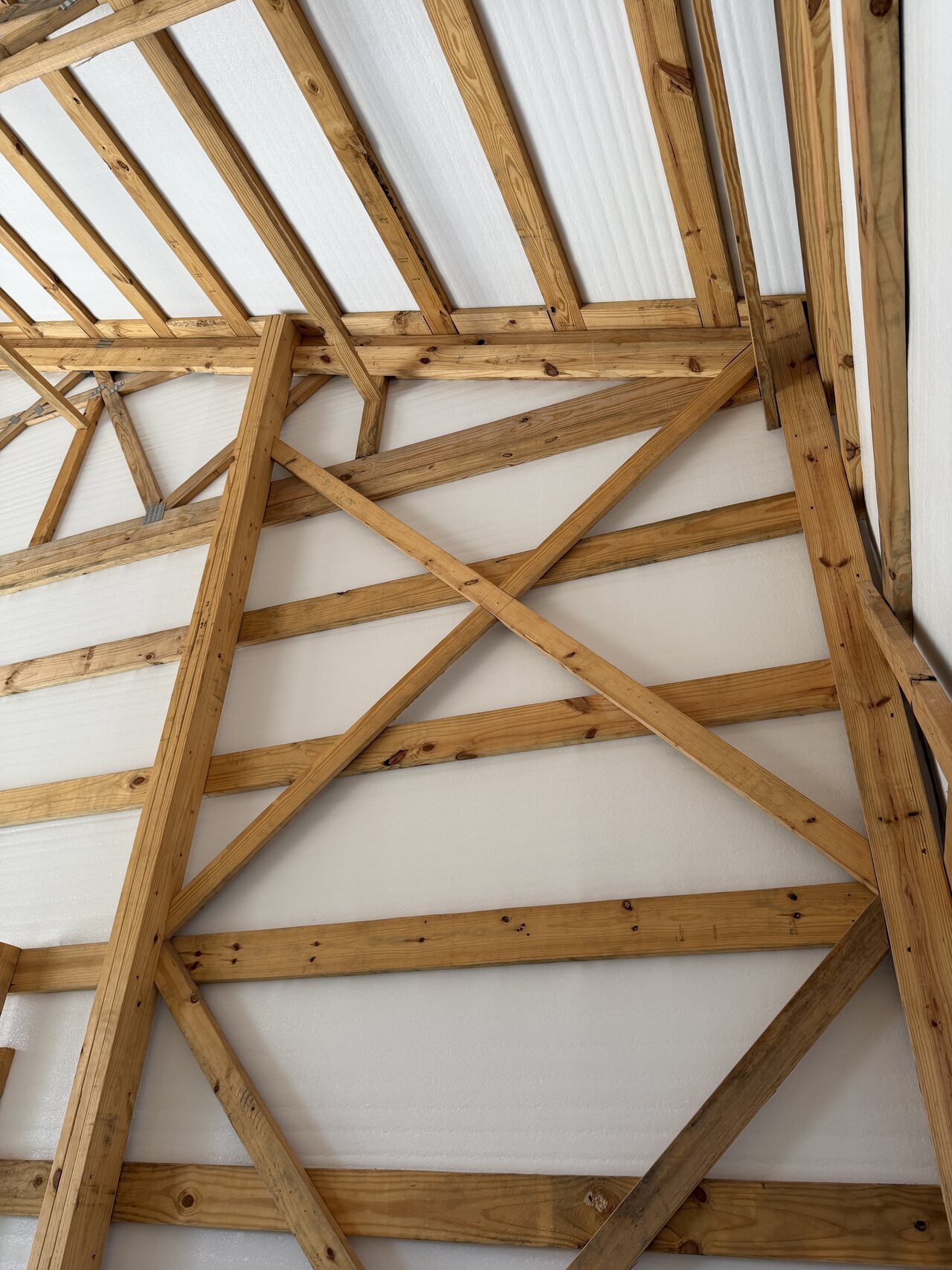 Upper barn gable with diagonal wood bracing, roof trusses, and white roof panels.