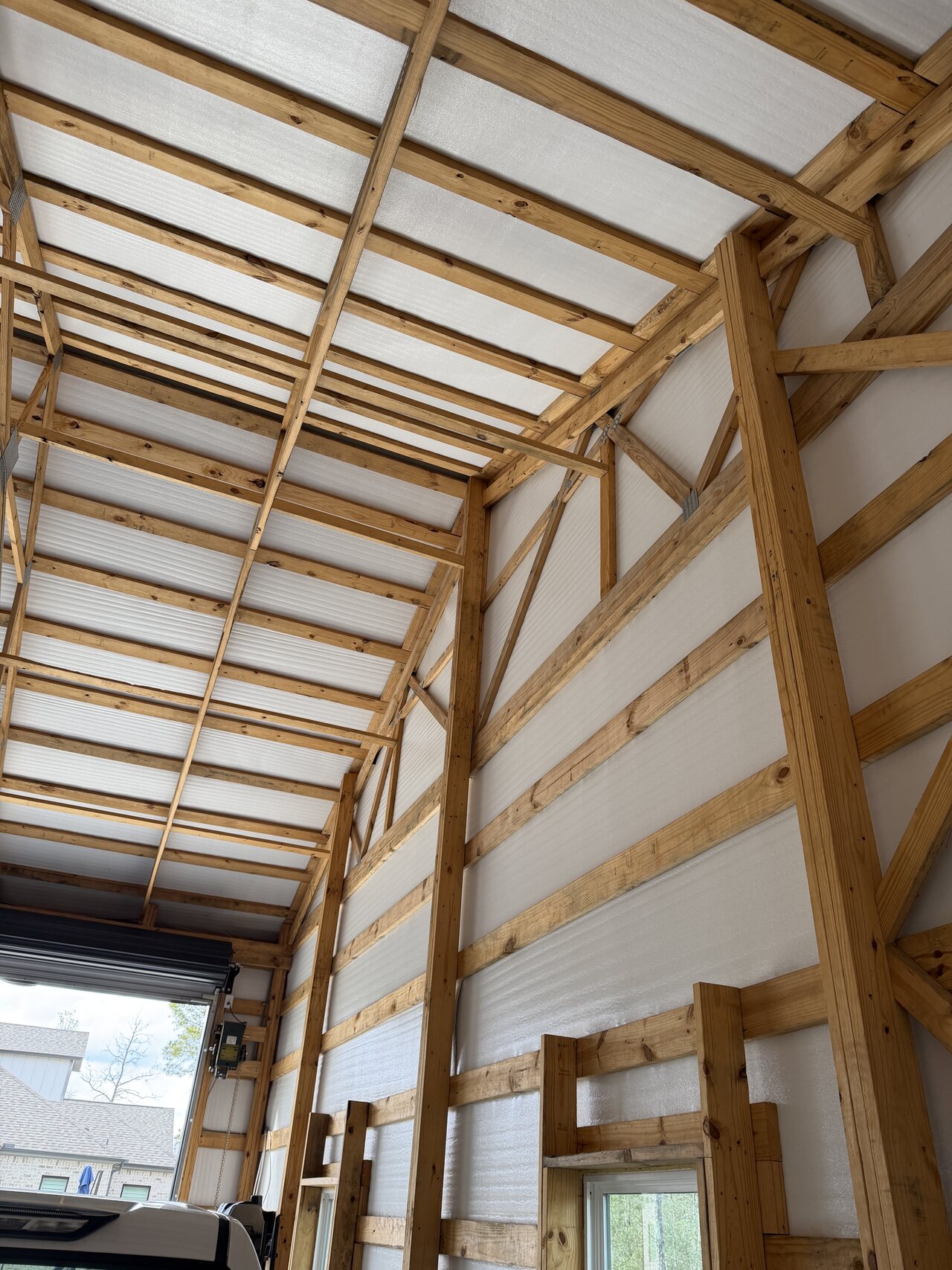 High barn wall and roof framing with repeated wood trusses and white panel surfaces.