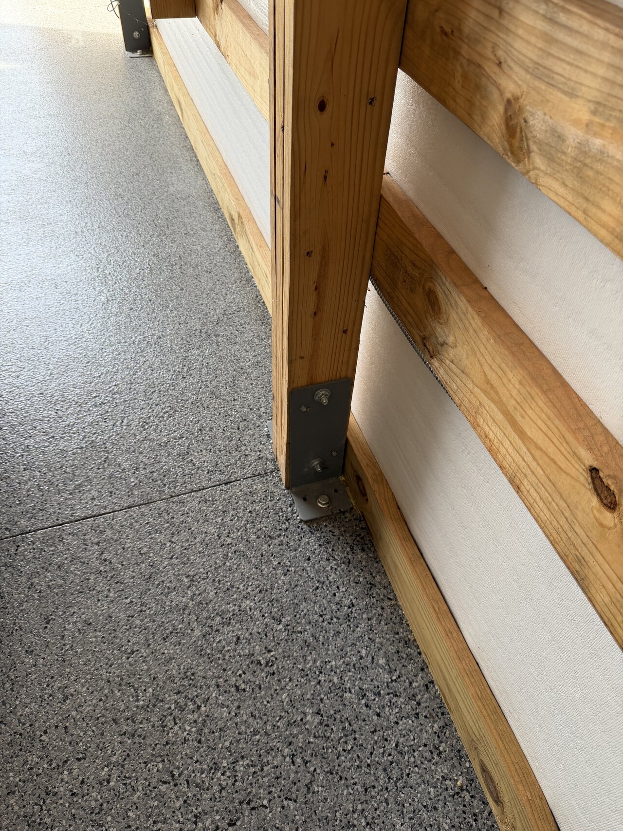 Close view of a barn post, base rail, lower wall panel, and concrete floor transition.