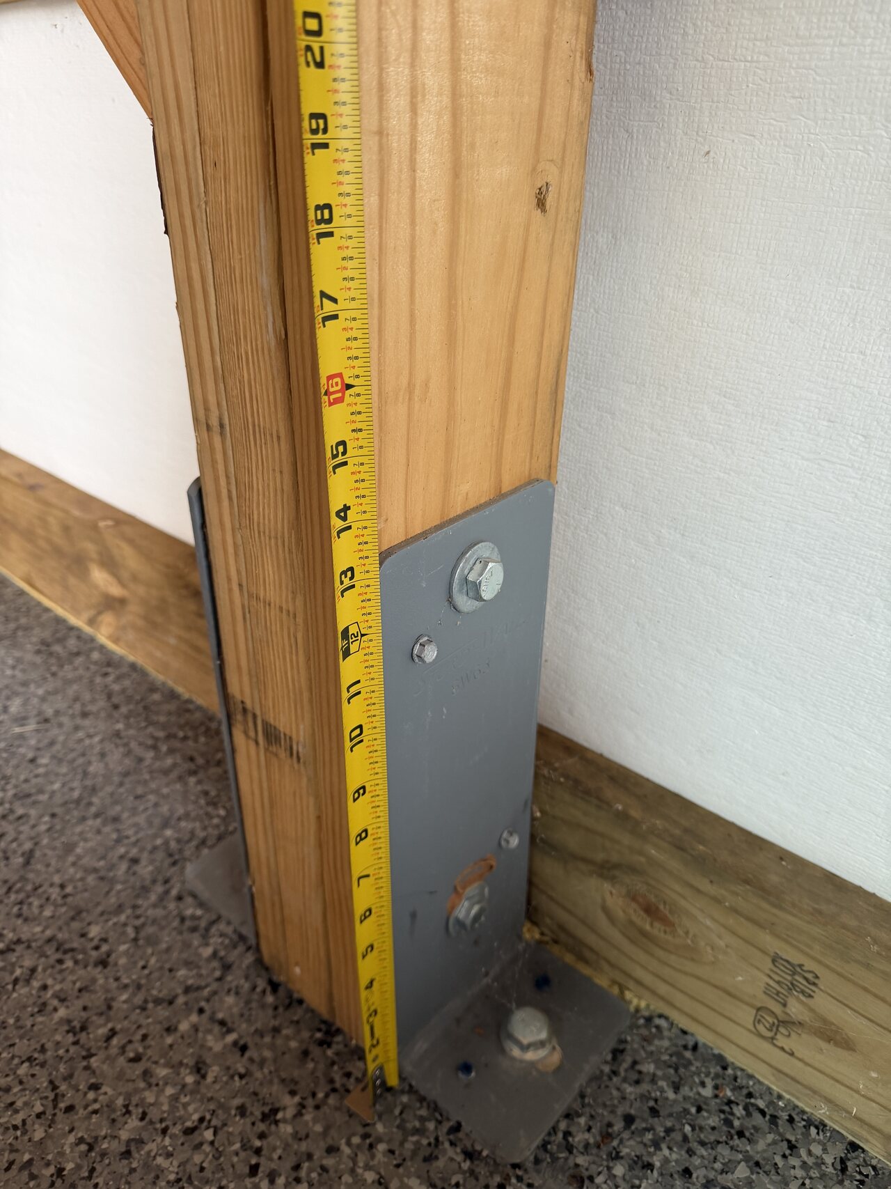 Tape measure held beside a metal post-base bracket and natural wood post at the barn wall.