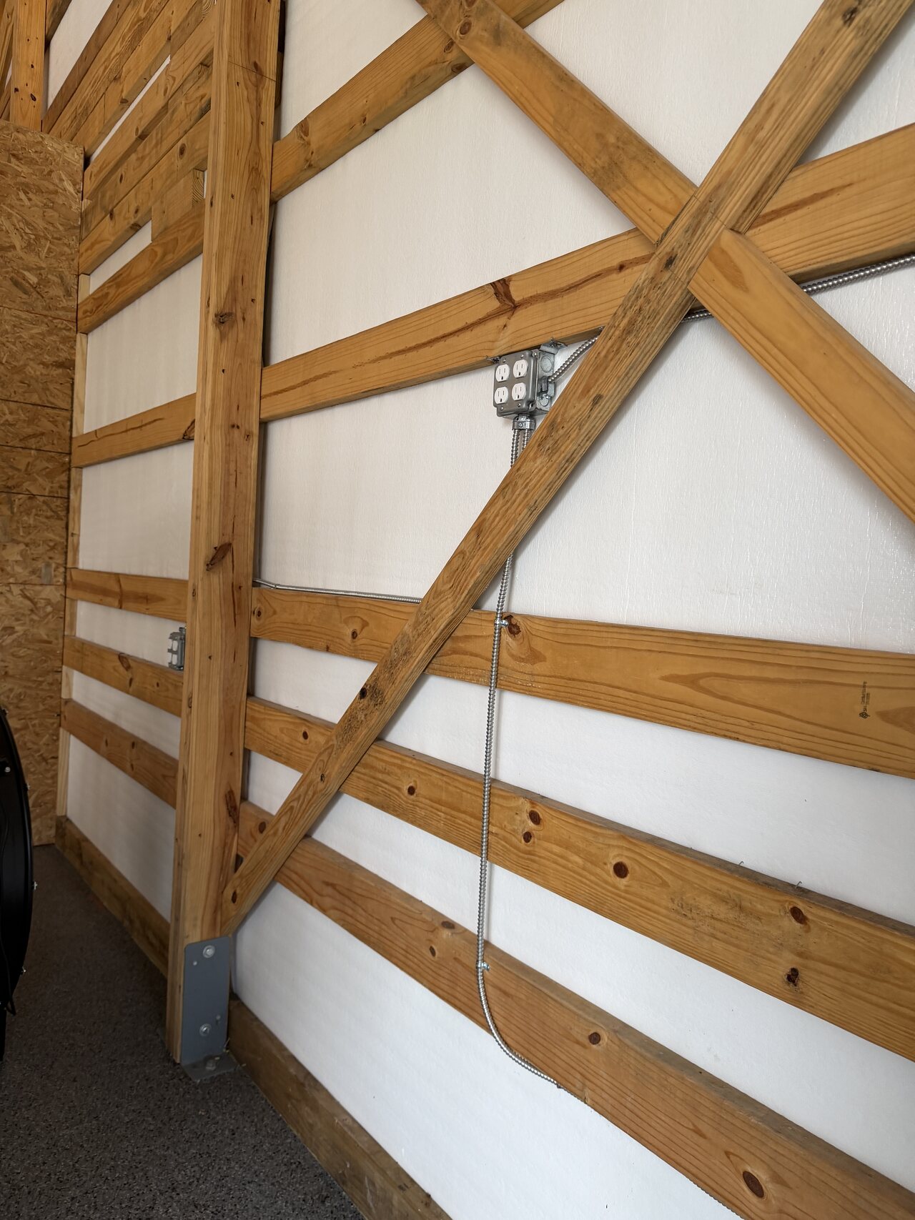 Diagonal barn wall bracing with a metal post-base bracket and repeated horizontal wood rails.