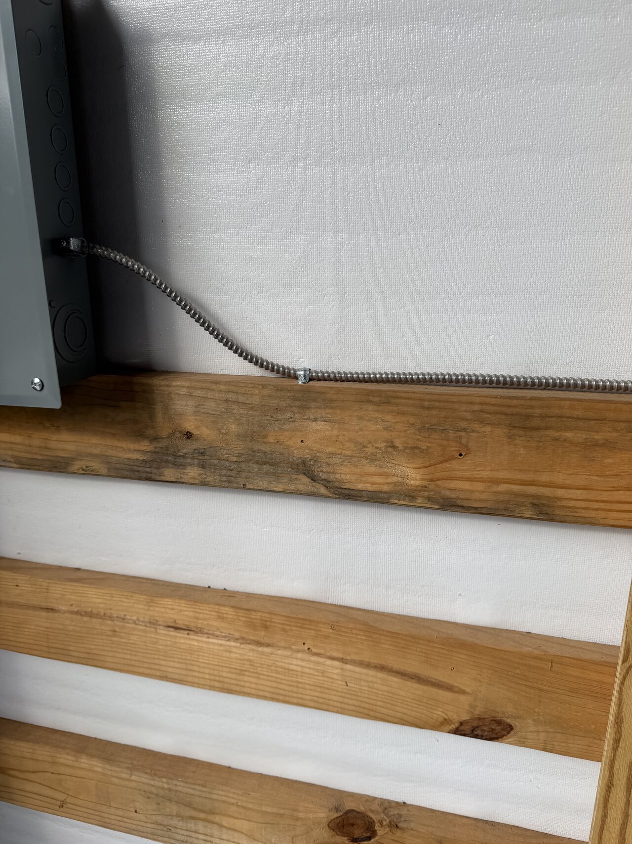 Close view of conduit and lower horizontal wood rails along a finished barn wall.