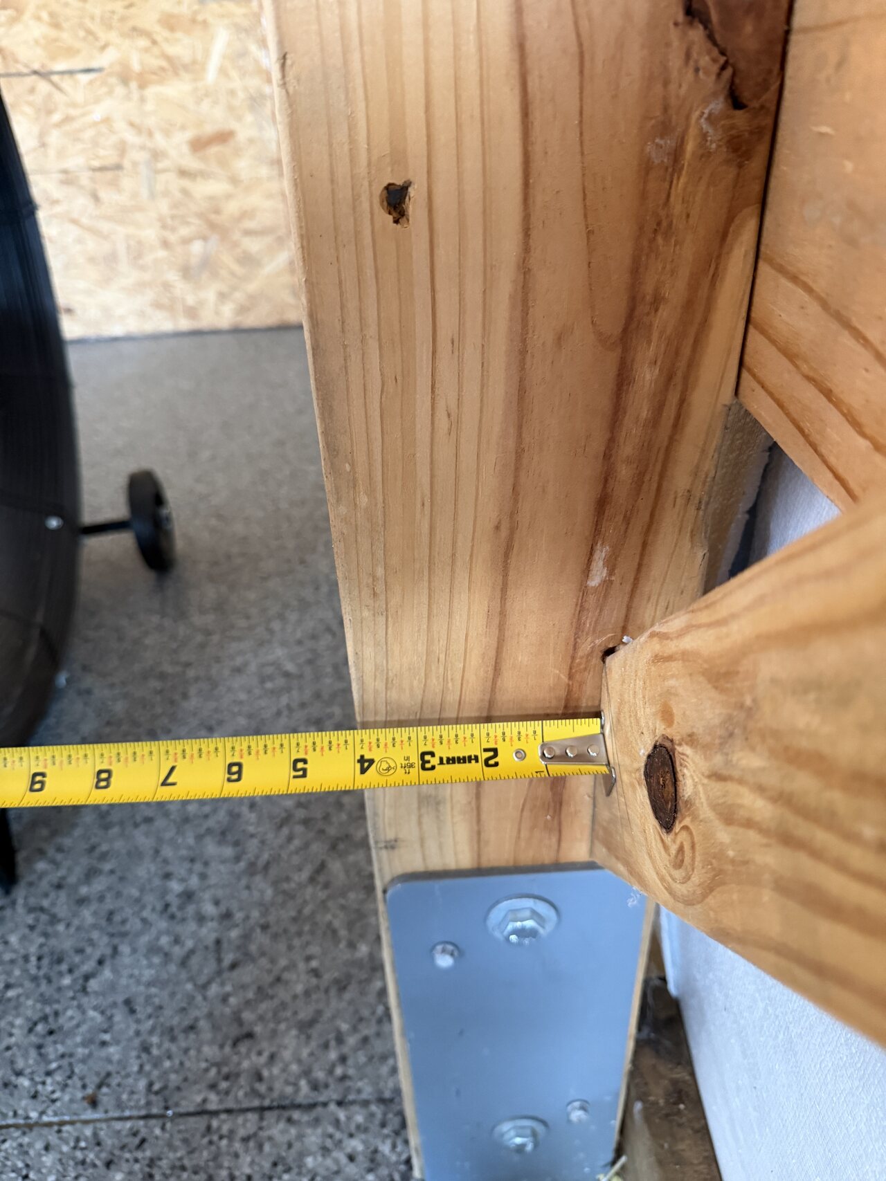 Tape measure check at a barn post-base bracket beside natural wood framing.