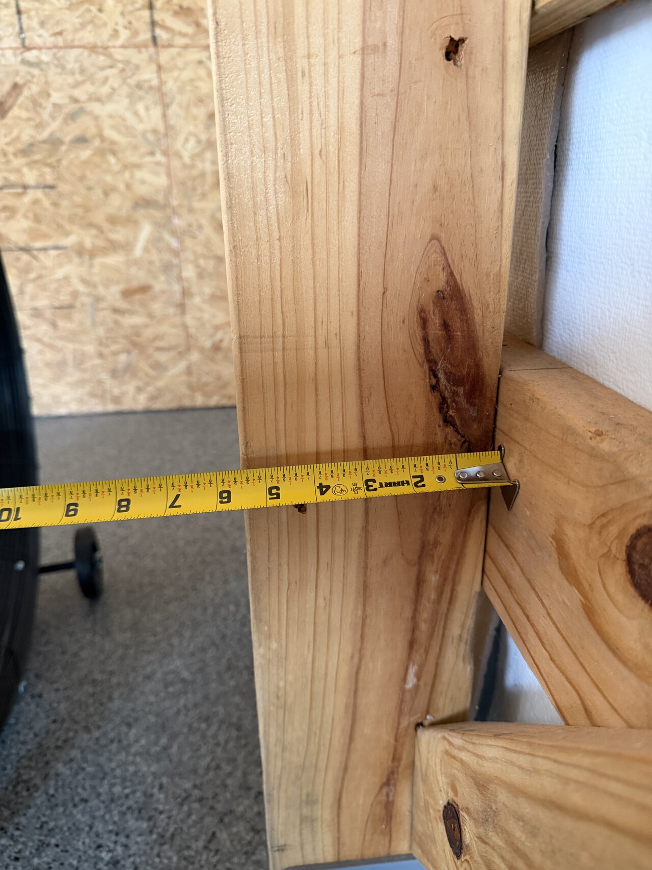 Tape measure stretched between barn wall framing members near a post and lower rail.