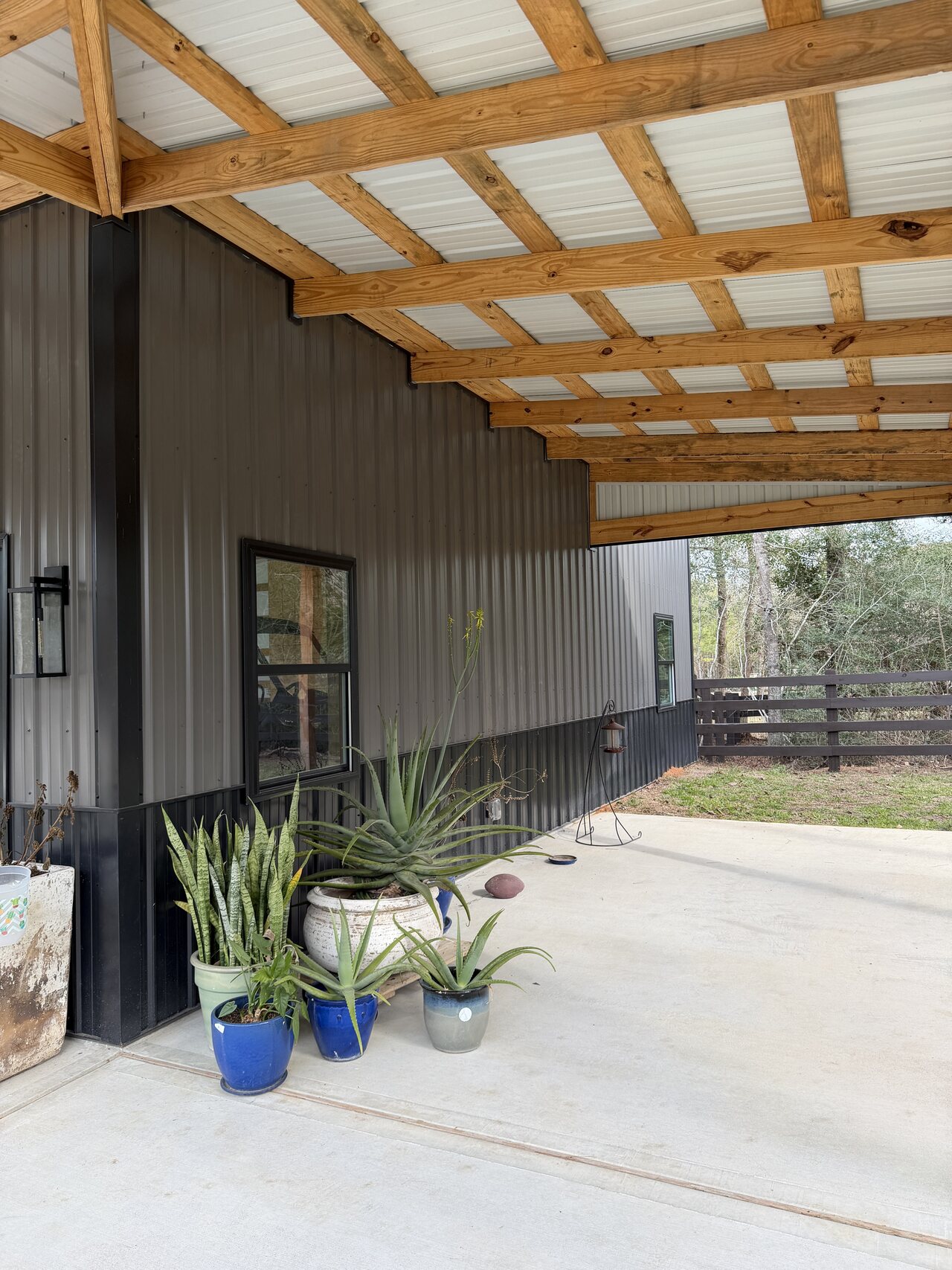 Covered exterior wall and porch area with wood posts, dark metal siding, and concrete surface.