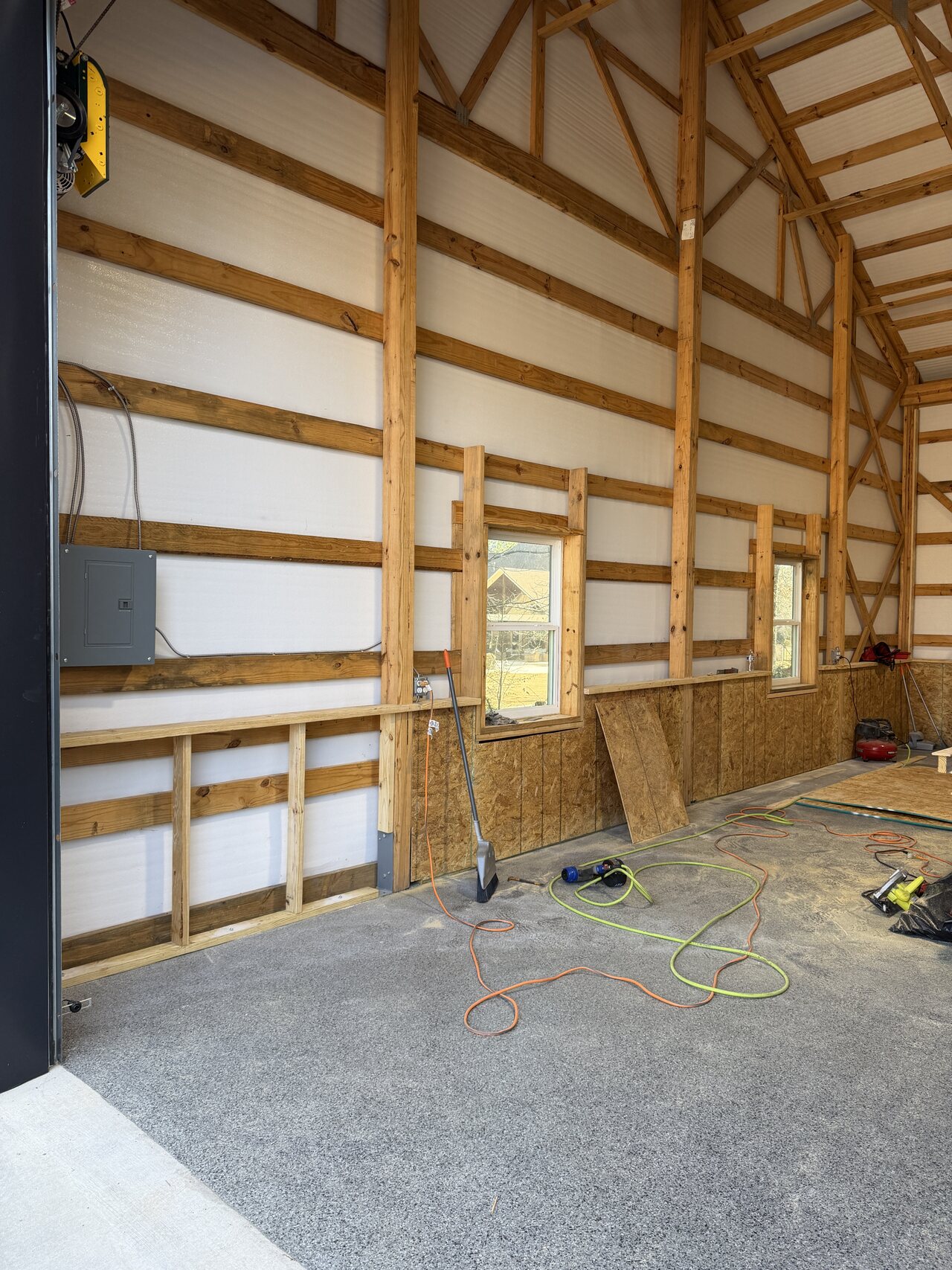 In-progress barn interior with exposed wood wall grid, OSB lower panels, tools, and concrete floor.