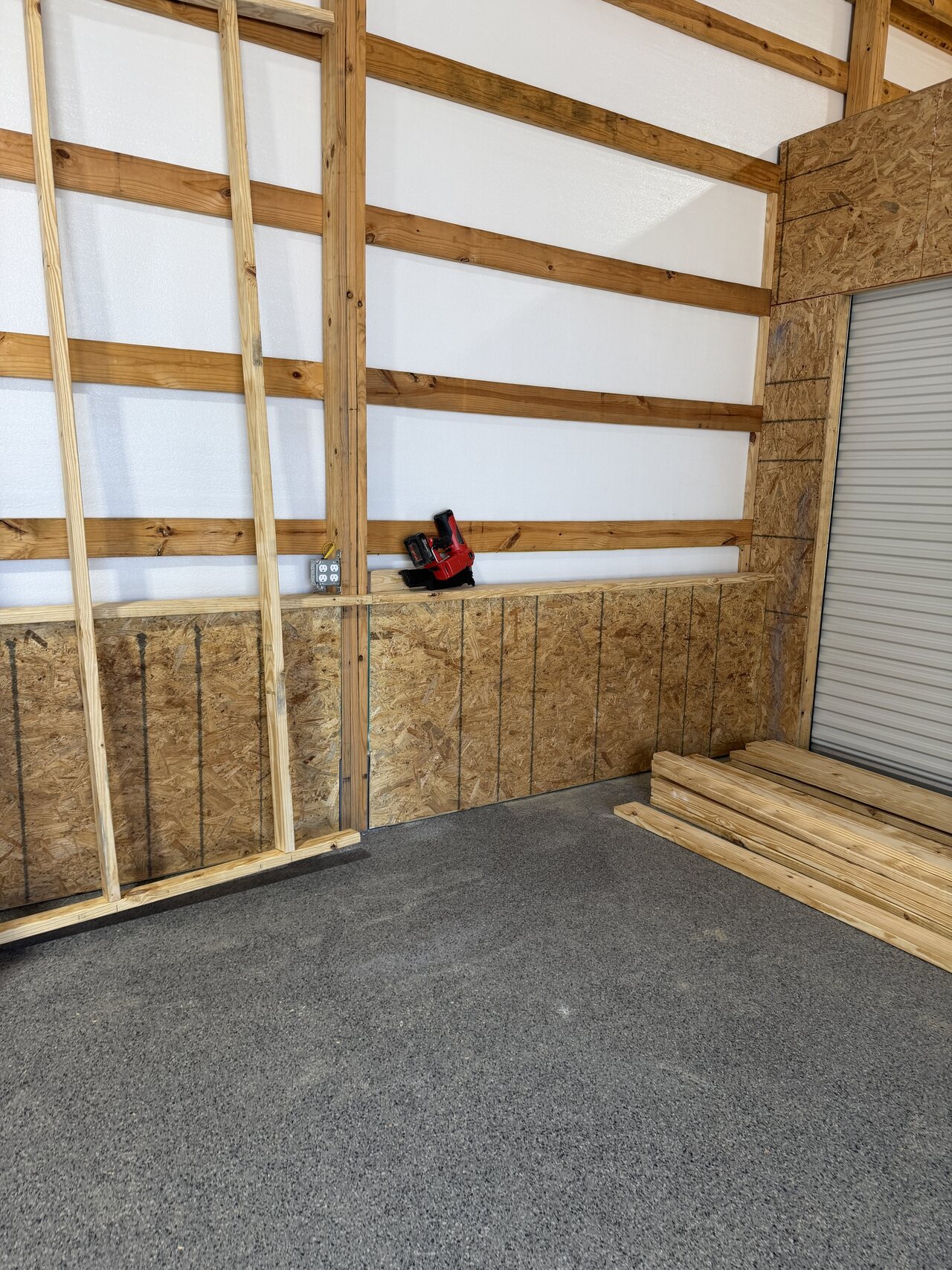 Barn interior corner with OSB lower wall panels, horizontal wood boards, and staged trim material.