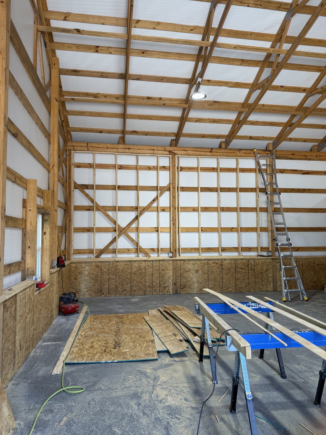 Framed lower barn wall with OSB panel work, open bay, staged material, and concrete floor.