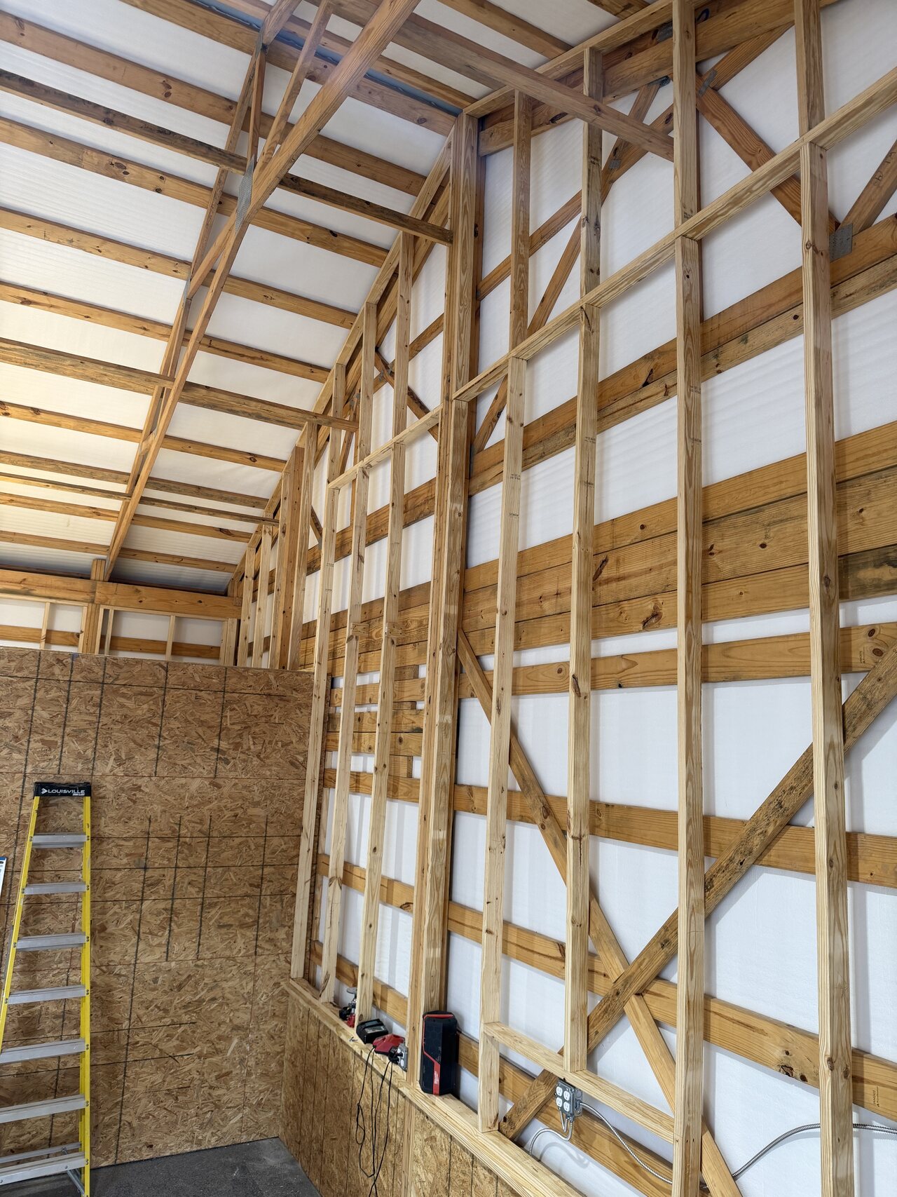 Tall framed barn wall section built over existing horizontal wood structure and lower panels.