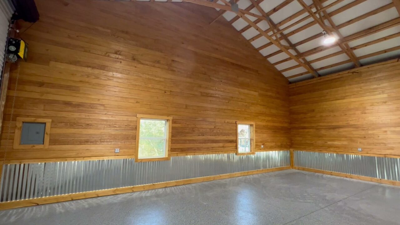 Finished barn interior with warm wood walls, exposed trusses, corrugated metal lower panels, and open concrete floor.