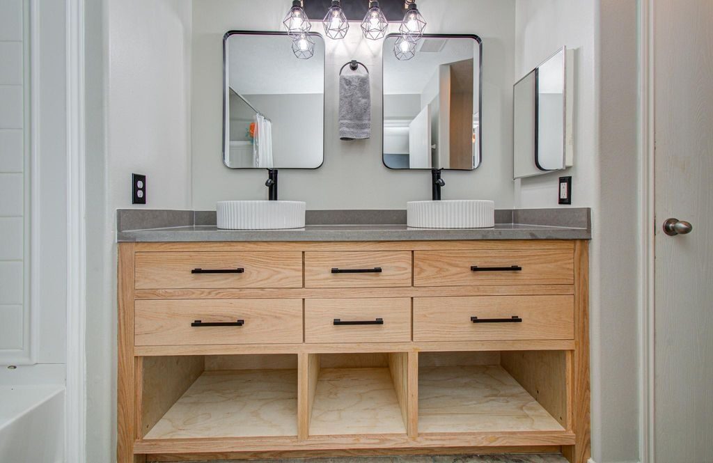 Finished double vanity with matching mirrors, open lower storage, and light wood cabinet faces reviewed after installation for a Joel Hodge project.
