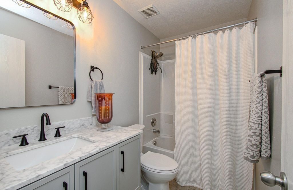Completed bathroom view showing the vanity run, stone counter, mirror line, plumbing fixtures, and adjacent wet-area finish coordination for a Joel Hodge project.