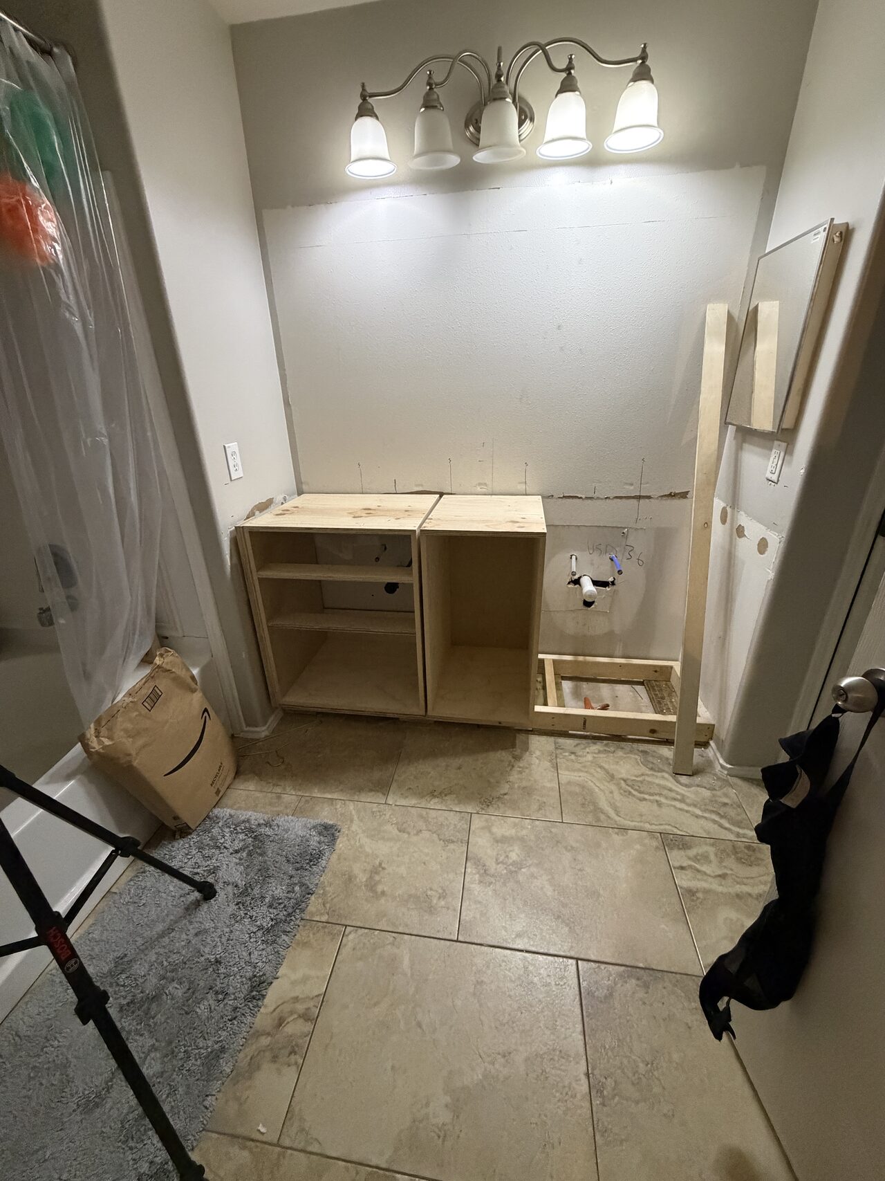 Unfinished vanity cabinet shell set in the protected bath work area while wall, light, and plumbing clearances were checked for a Joel Hodge project.