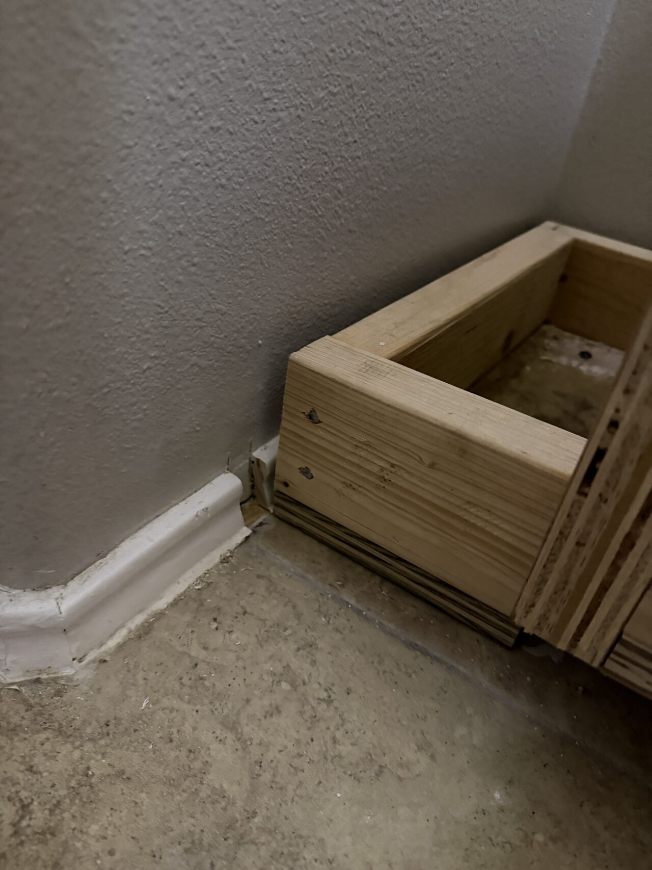 Light wood cabinet box being fit at the bathroom corner with floor protection and wall clearances visible for a Joel Hodge project.