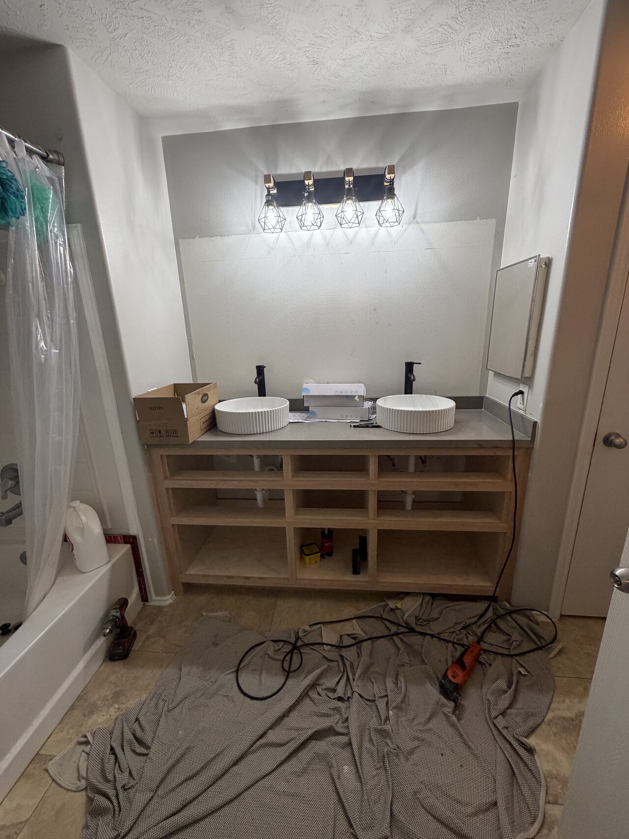 Vanity base installed before countertop and sinks, showing the drawer banks, open shelf layout, and cabinet-to-wall fit for a Joel Hodge project.
