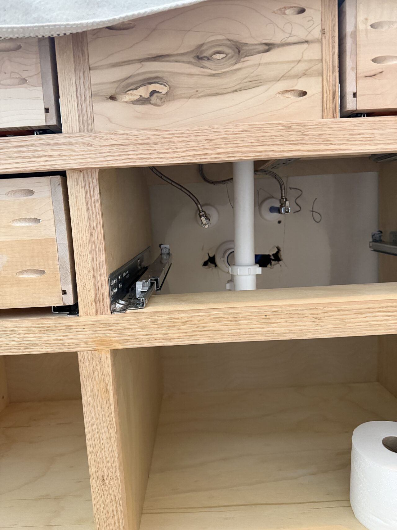 Close-up of the vanity interior and open shelf framing where plumbing clearance and usable storage were coordinated for a Joel Hodge project.