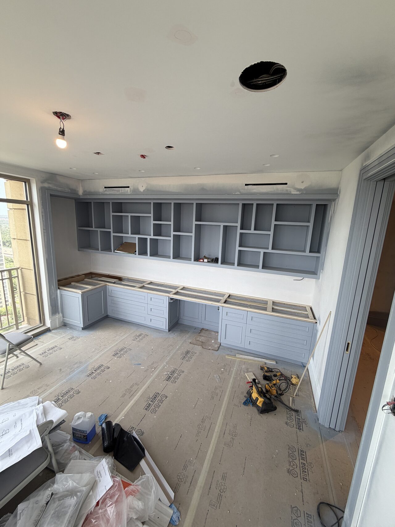 Painted built-in wall with upper cabinets, base storage, and room protection visible during final installation review for a Joel Hodge project.