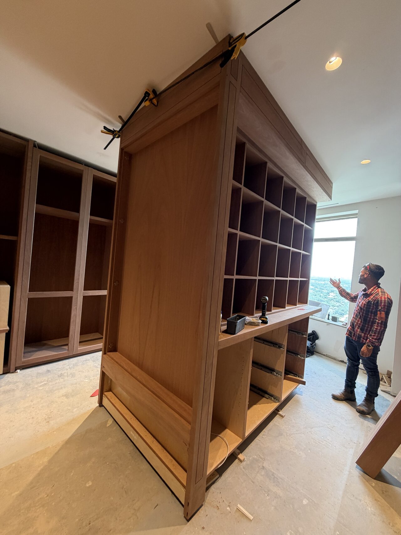 Large stained wood library unit during installation, showing tall panels, shelving, and field protection for a Joel Hodge project.