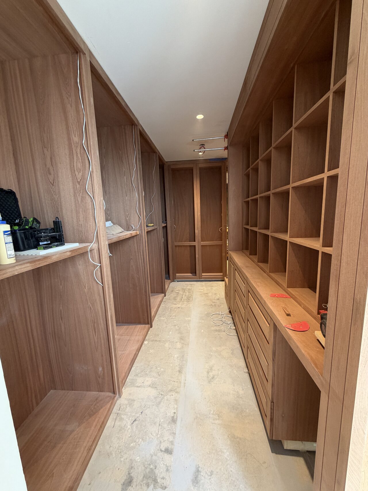 Long closet corridor showing matching wood shelving and drawers on both sides after installation for a Joel Hodge project.