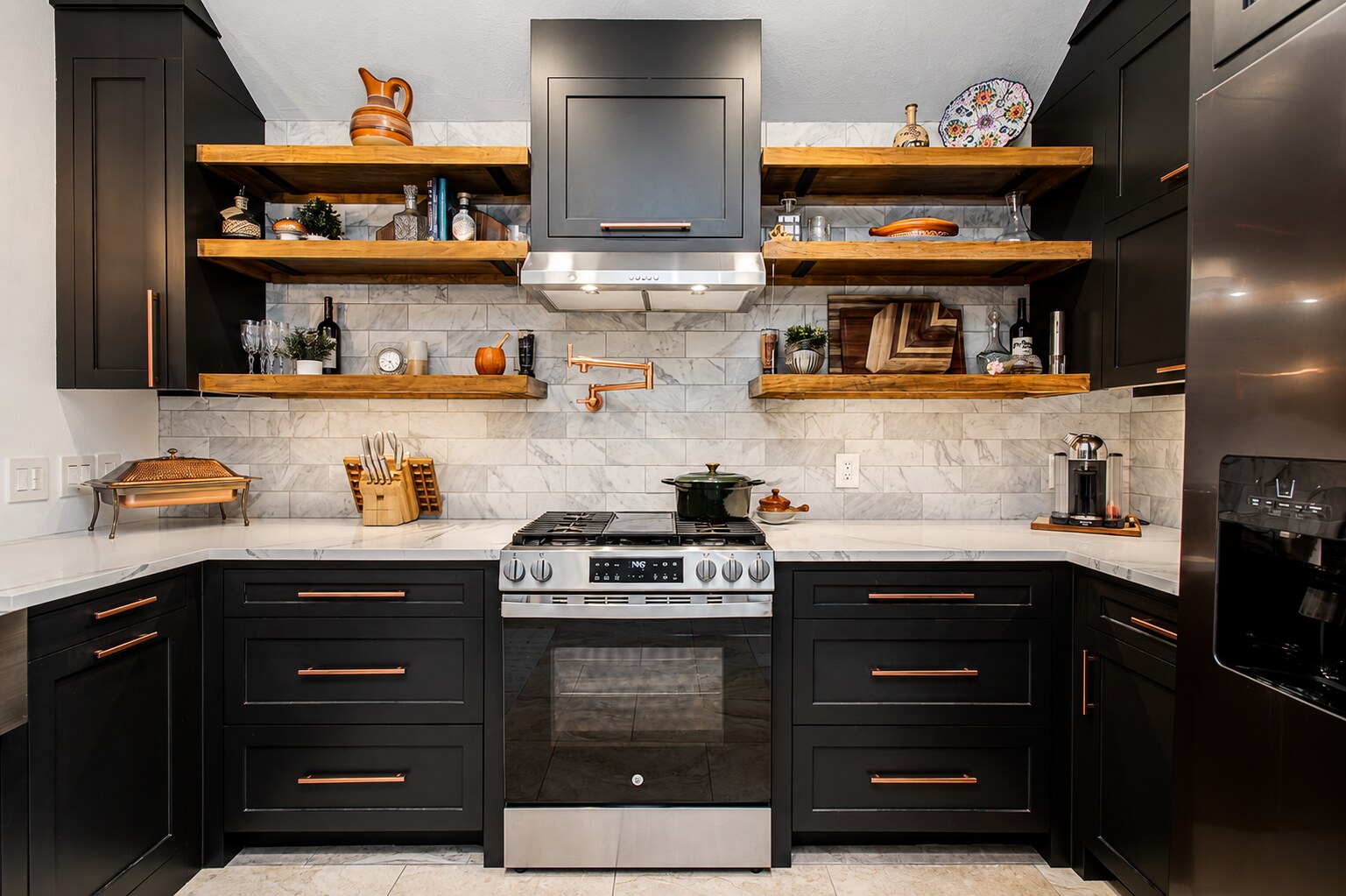 Completed dark kitchen with wood shelves, central range wall, hood, tile backsplash, dark cabinets, and copper-toned pulls.
