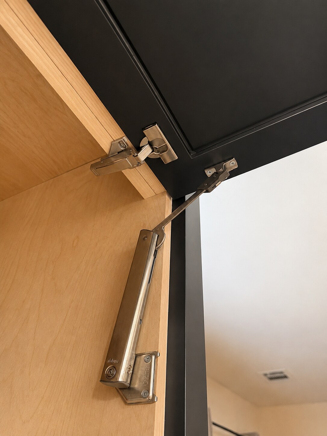 Close view of a light wood drawer box beside a dark finished cabinet panel and floor tile.