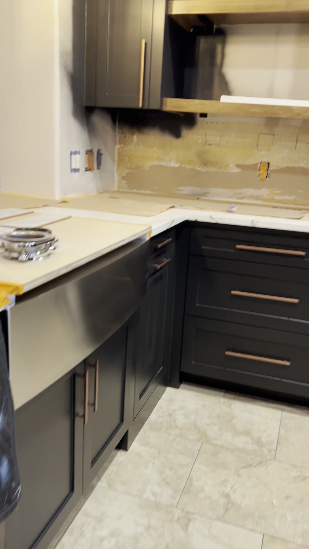 In-progress kitchen cabinet installation with dark base cabinets, protected counters, exposed backsplash area, and electrical openings.