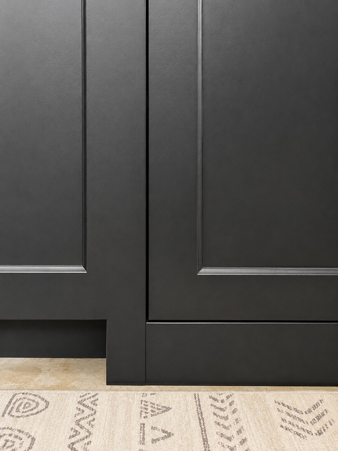 Close view of dark base cabinet doors aligned above a toe-kick area at the finished floor line.