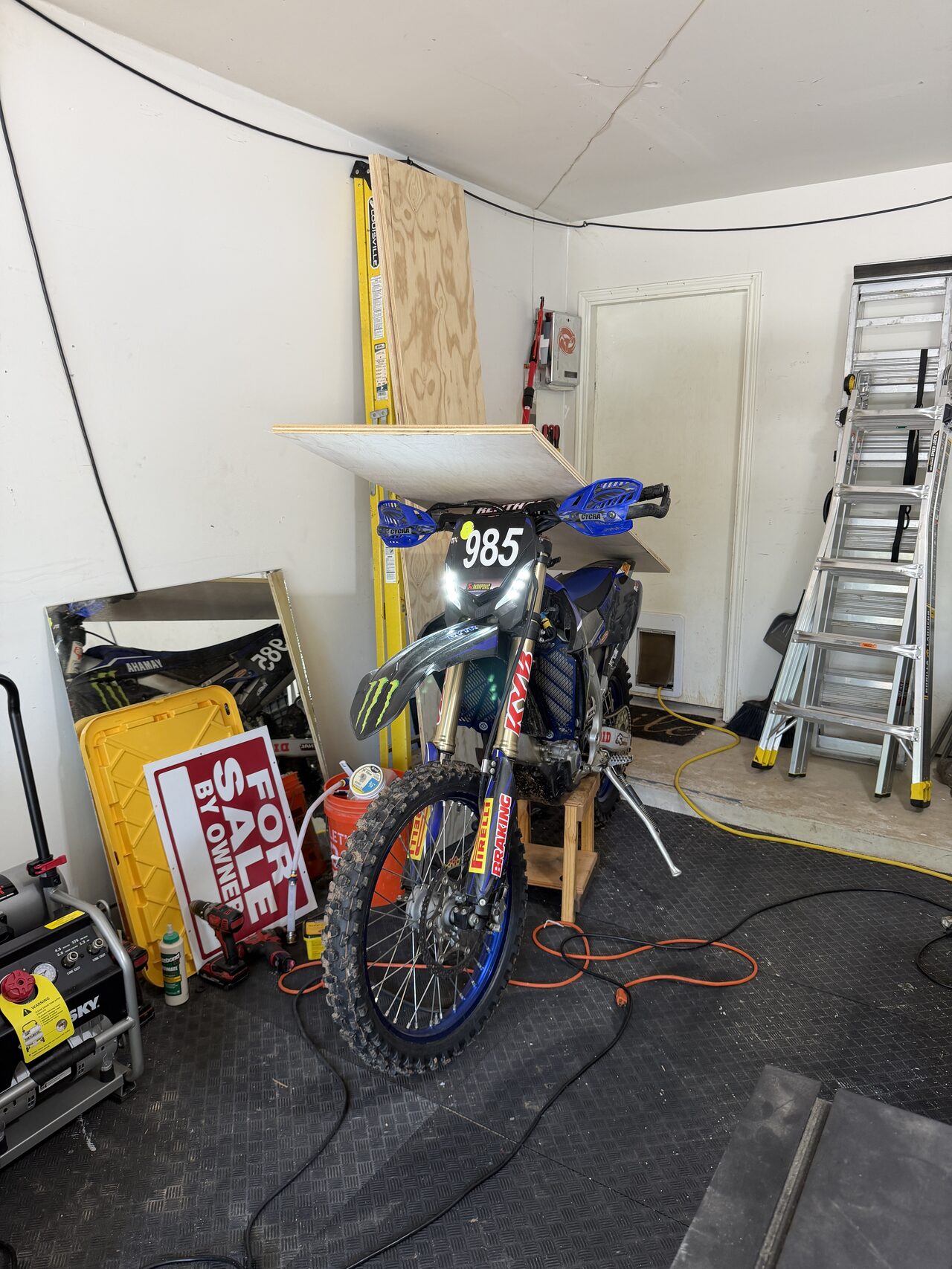 Garage work area with ladder and wall opening visible during door and trim coordination for a Joel Hodge project.