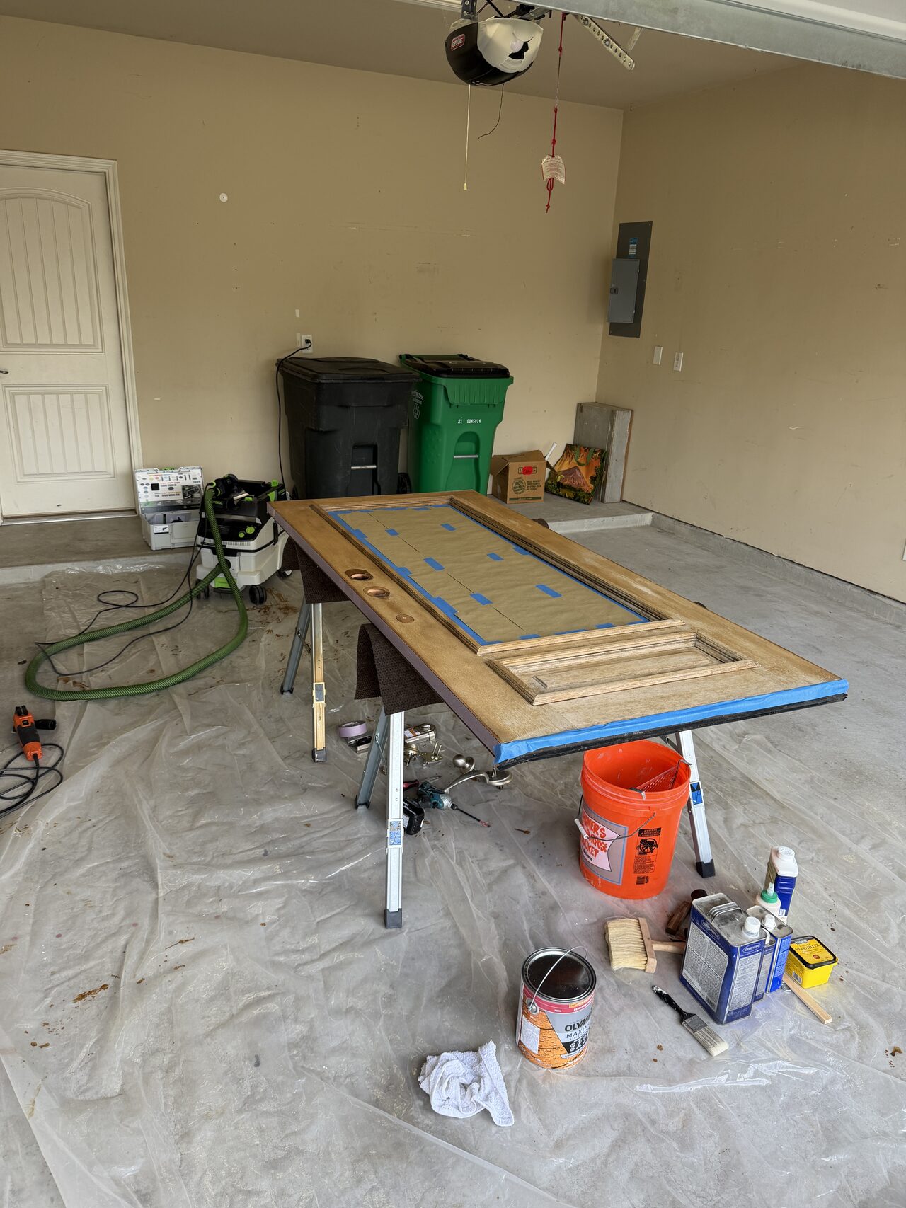 Garage refinishing setup with the door on sawhorses and finish materials staged nearby for a Joel Hodge project.