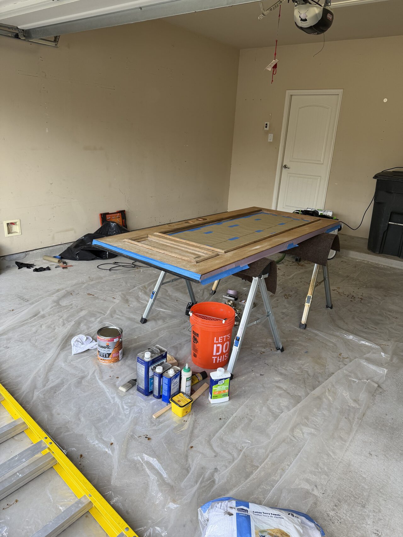 Protected garage floor and door refinishing work area set up before stain and finish application for a Joel Hodge project.