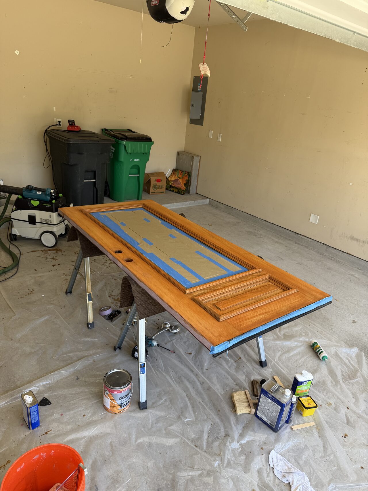 Taped door slab during refinishing with glass protected and raised panels ready for coating for a Joel Hodge project.