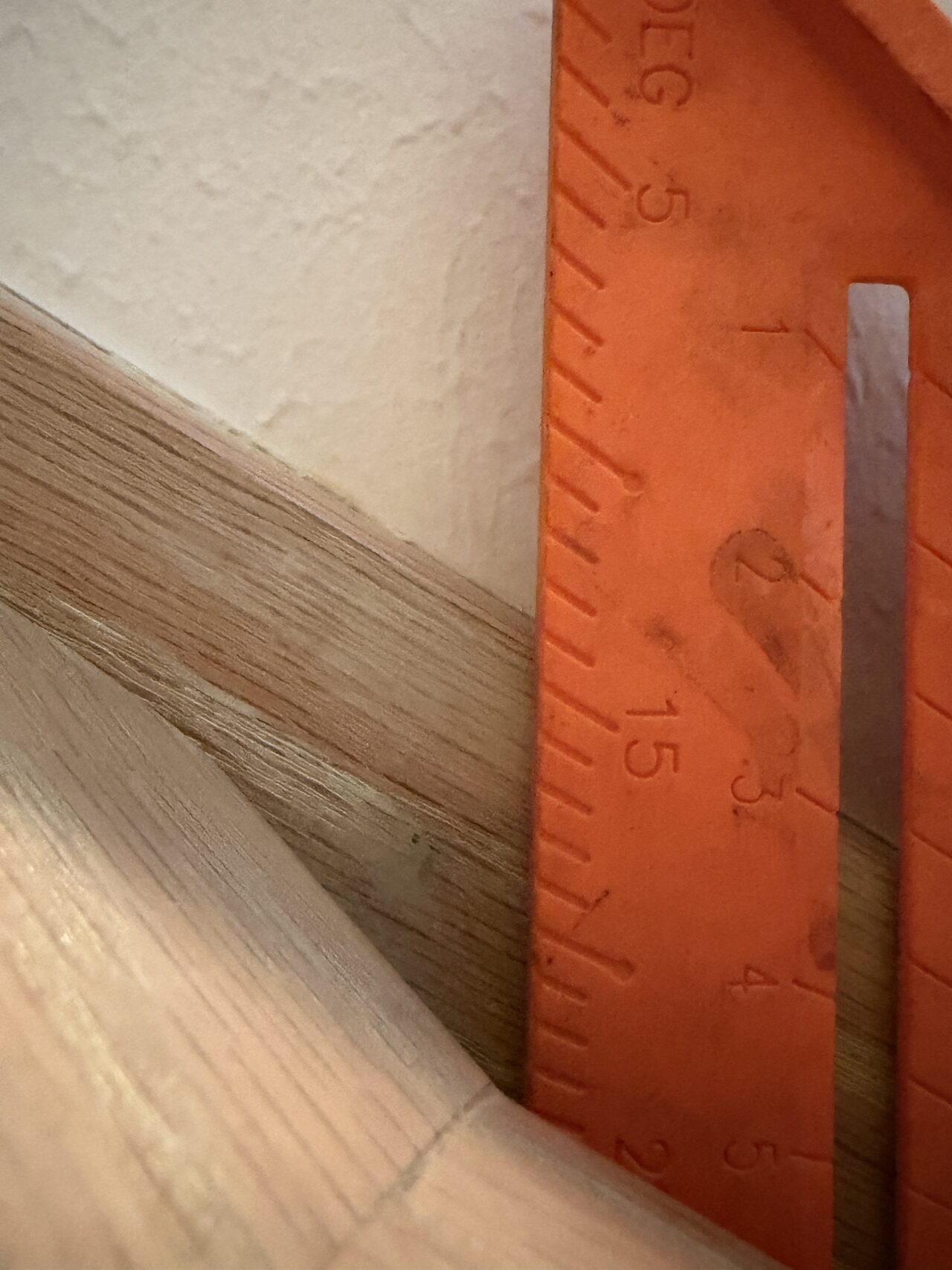 Riser and trim depth checked against the wall with a ruler before stair finish adjustments for a Joel Hodge project.