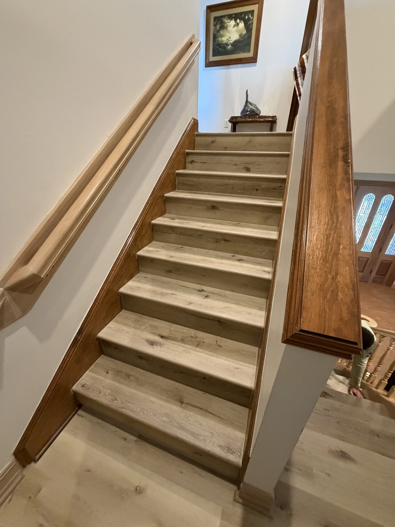 Lower stair view showing refreshed treads, risers, handrail, and base trim coordination for a Joel Hodge project.