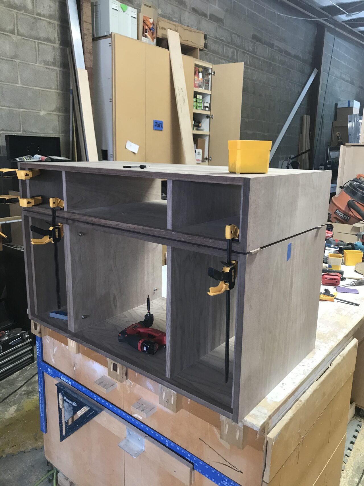 Side view of the dark outer cabinet shell clamped on the bench during assembly for a Joel Hodge project.