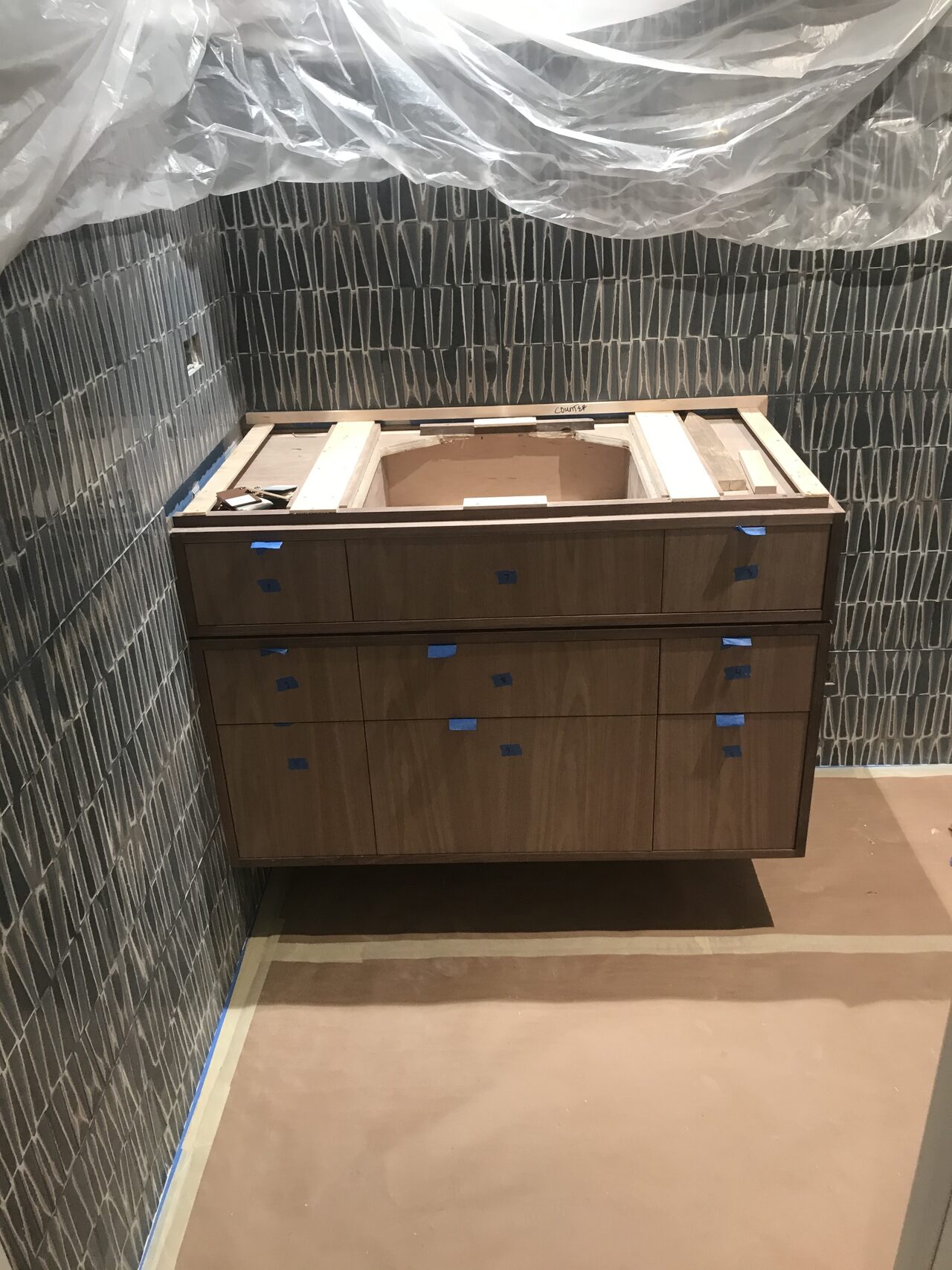 Vanity set in the bathroom alcove before countertop installation, with wall protection in place for a Joel Hodge project.
